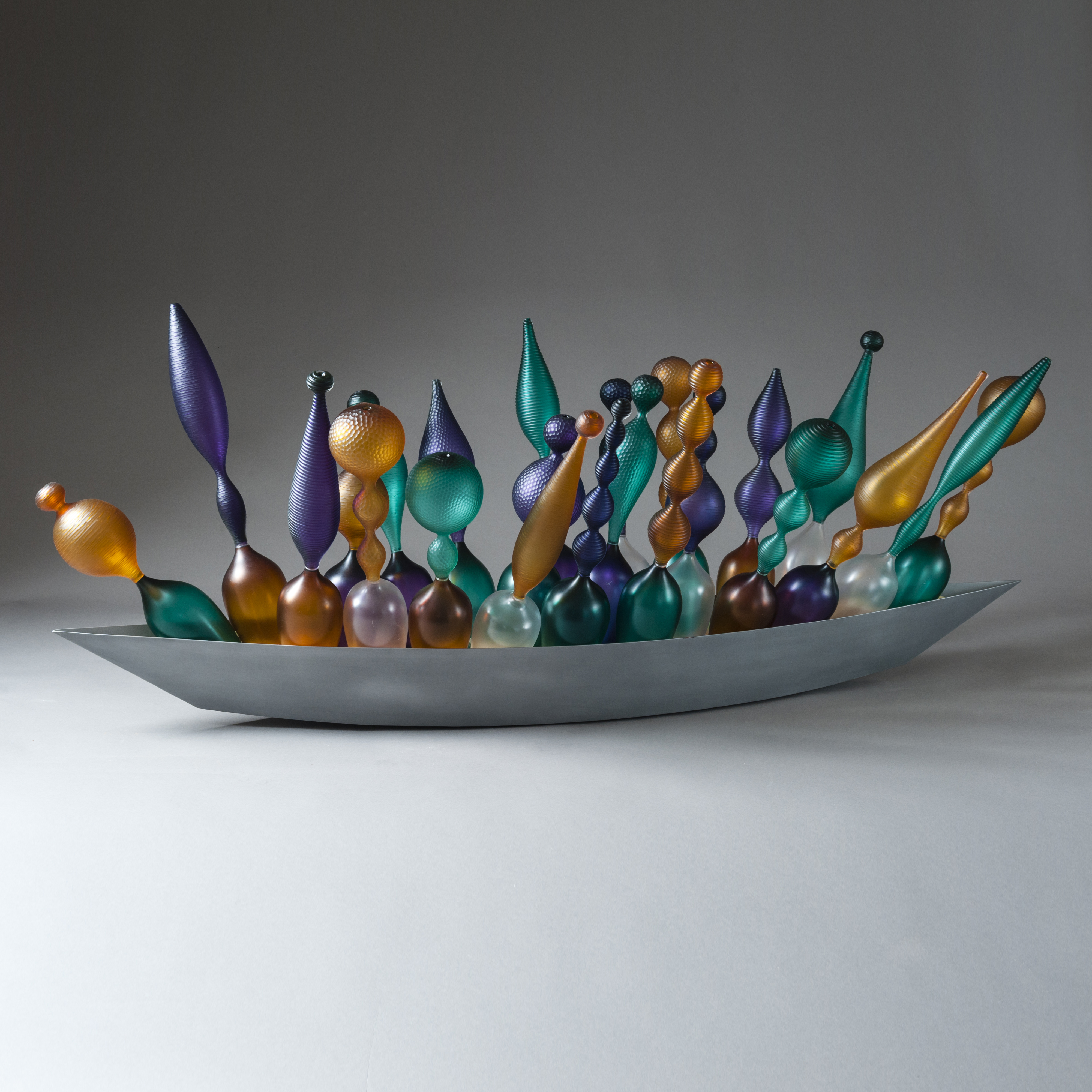 thin art glass sculpted objects in orange purple and green in long grey tray