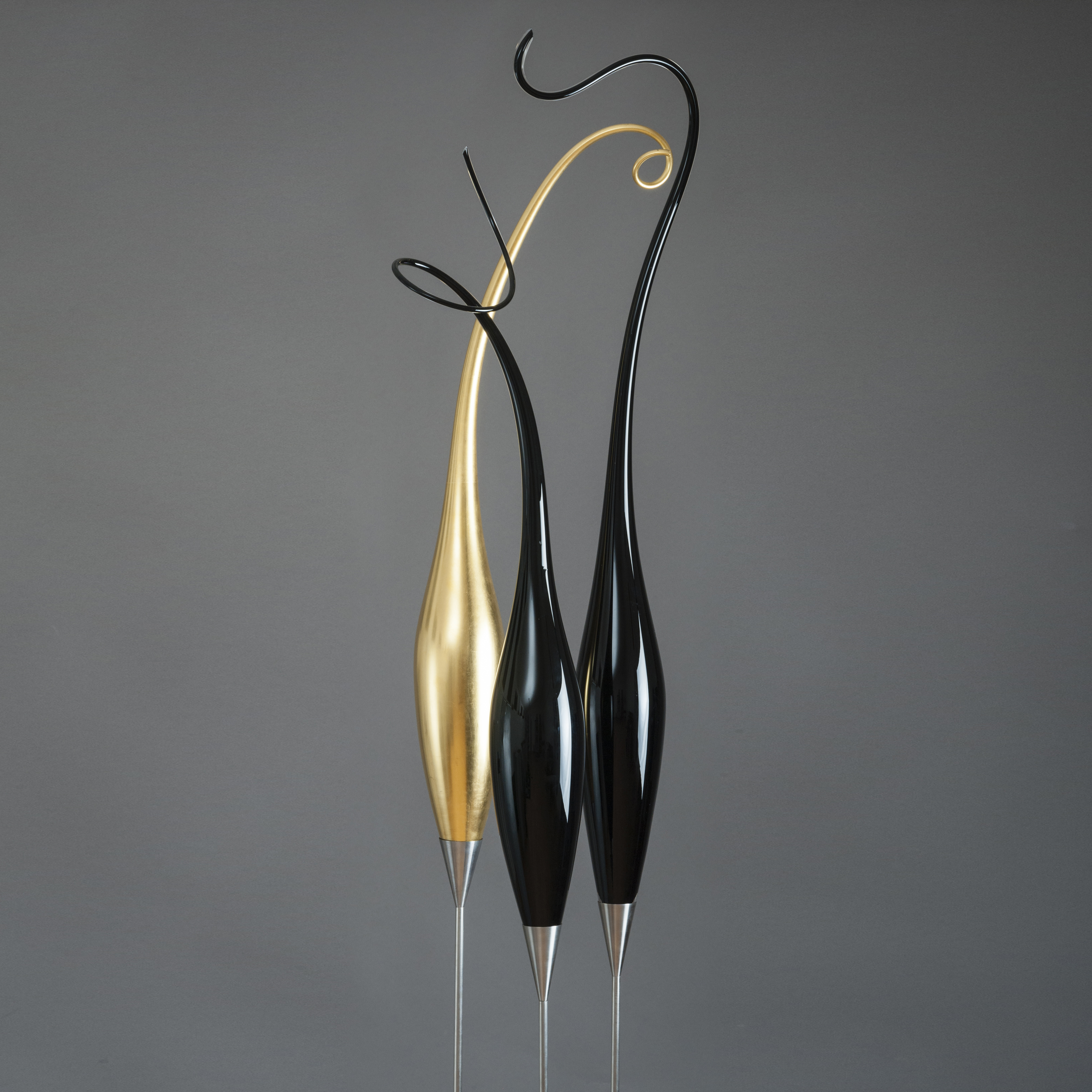 three tall thin glass art strands in black and gold on steel stick bases