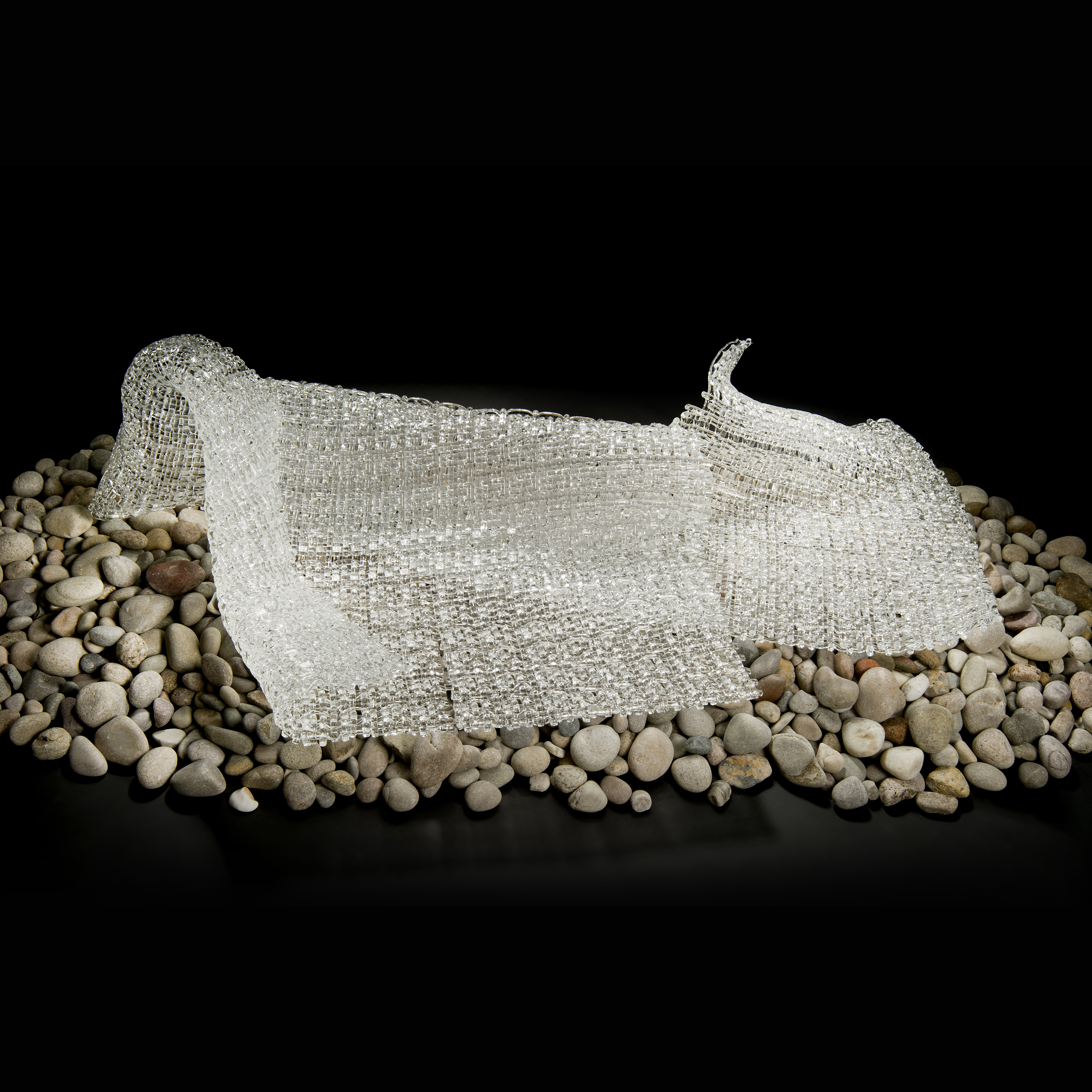 layered art glass sculpture resembling cloth on pebble base