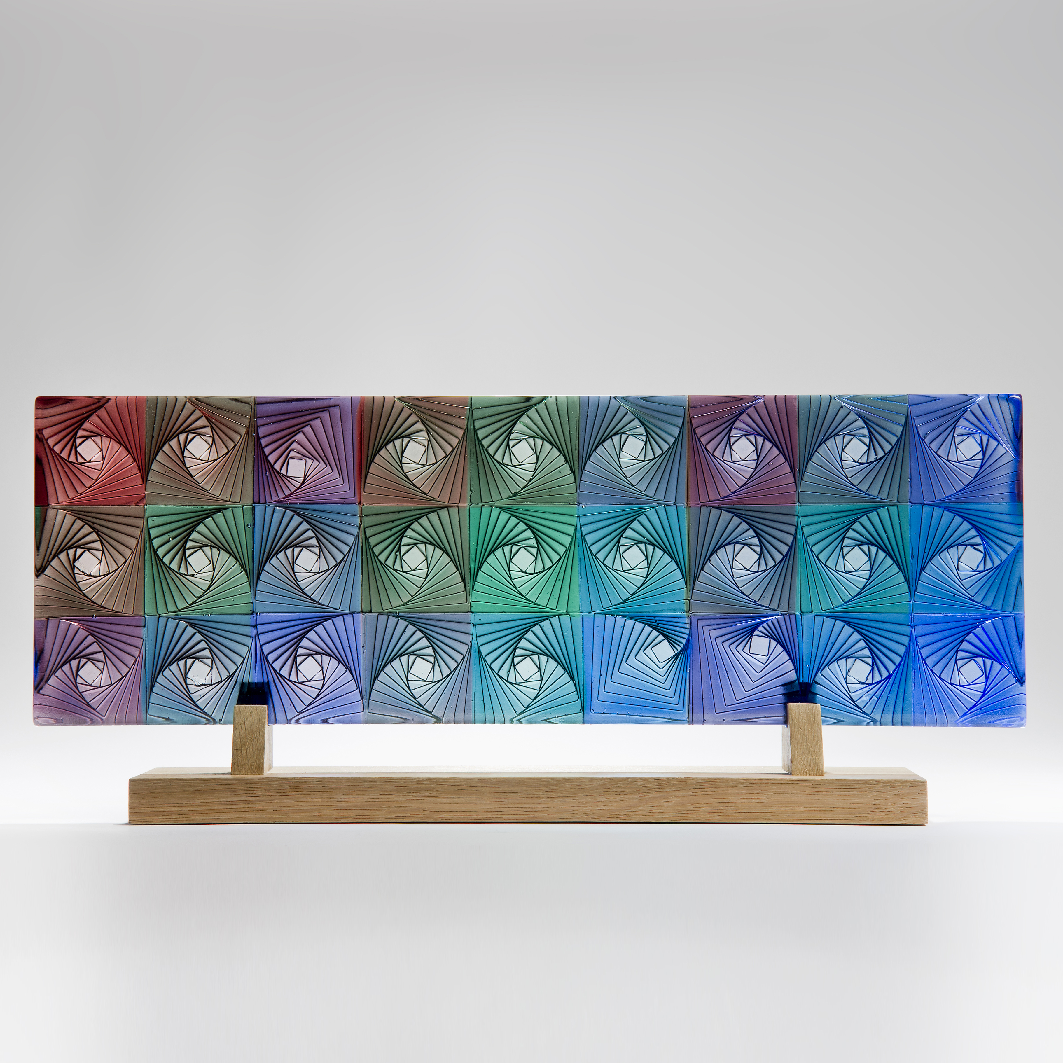colourful flat rectangular cast glass sculpture resting on wooden base