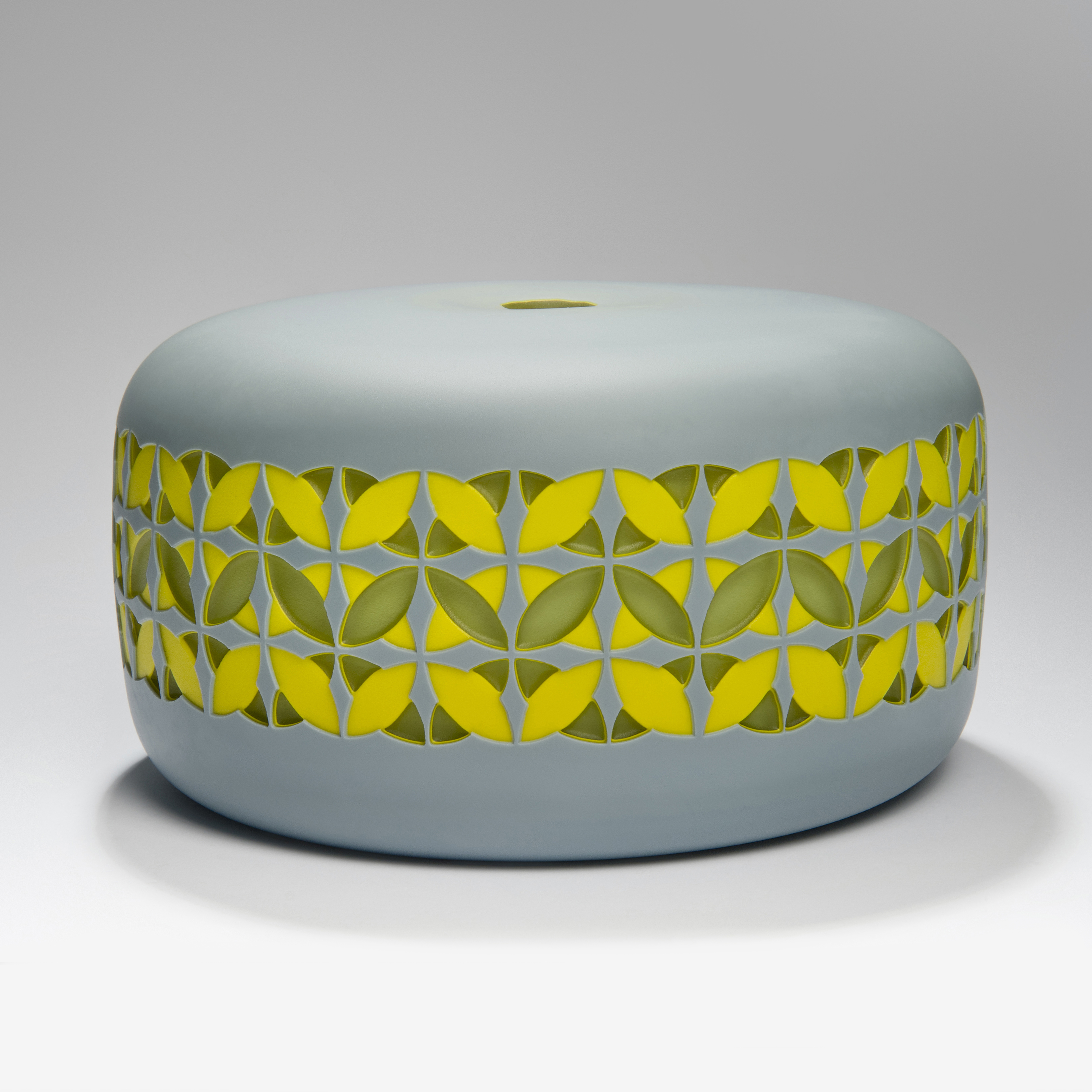 round cake shaped glass sculpture in grey with yellow and gren pattern