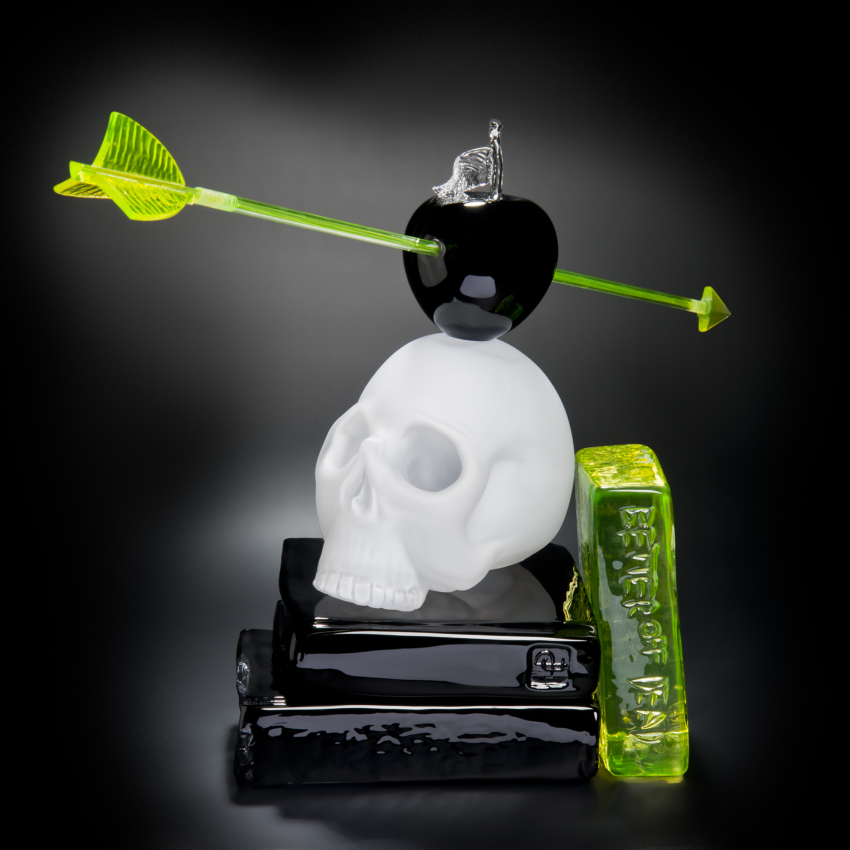 art glass still life sculpture of white skull on black base with neon green arrow through black apple resting on top