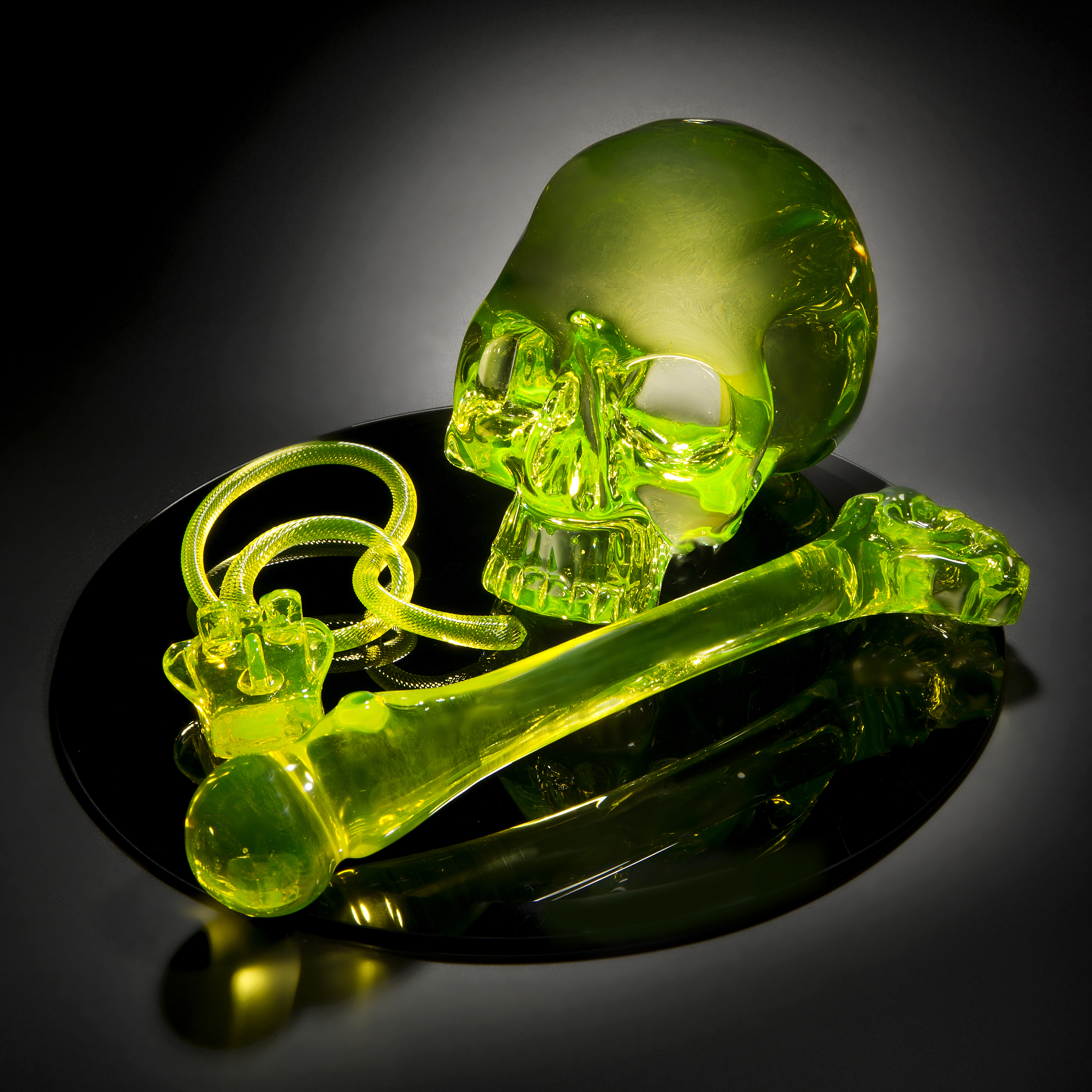 neon green coloured art glass sculpture of skull and bone on black mirror base