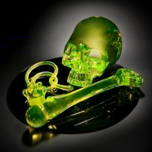 neon green coloured art glass sculpture of skull and bone on black mirror base