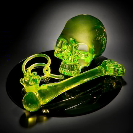 neon green coloured art glass sculpture of skull and bone on black mirror base