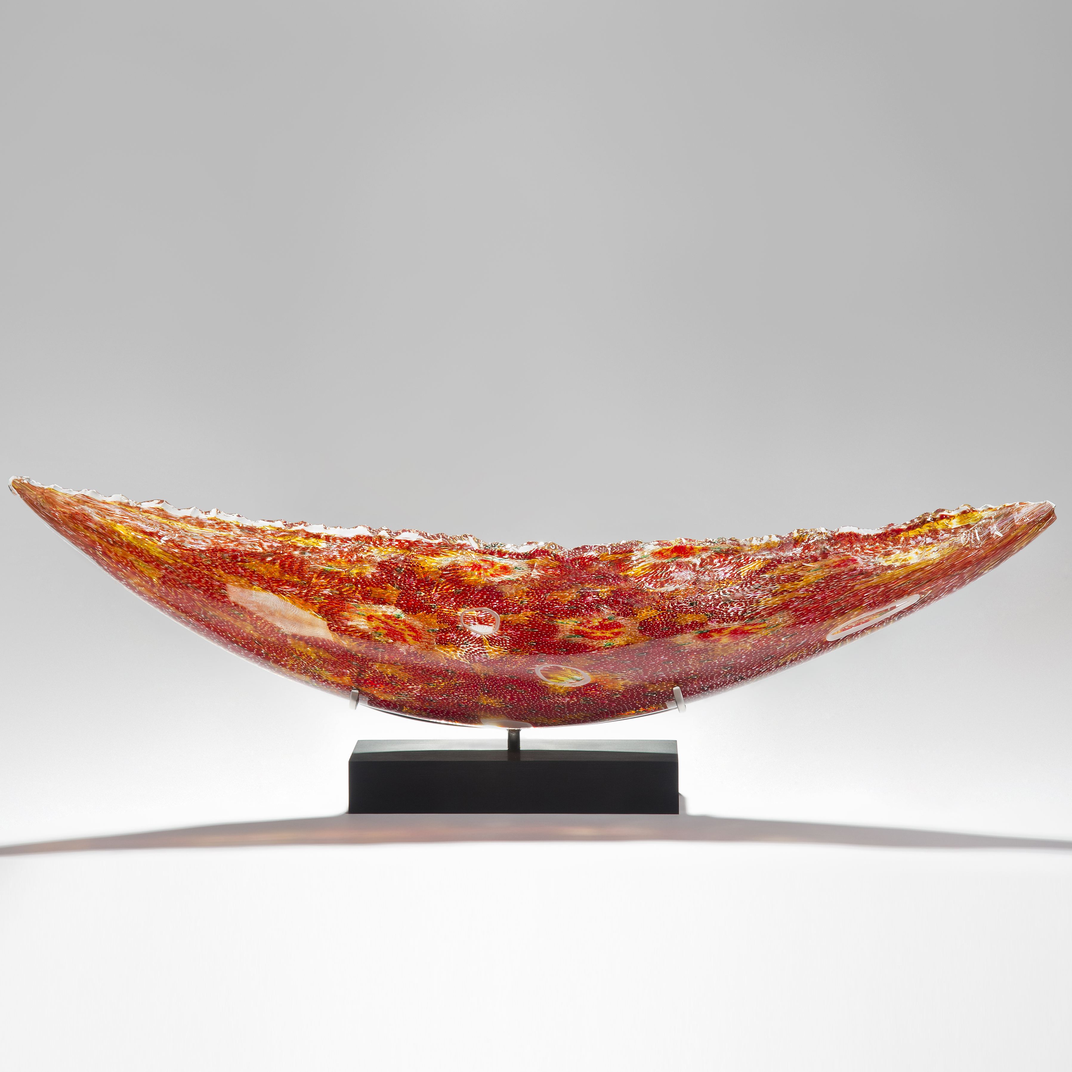 solid glass art sculpture in concave shape with detailled patterns in red and yellow