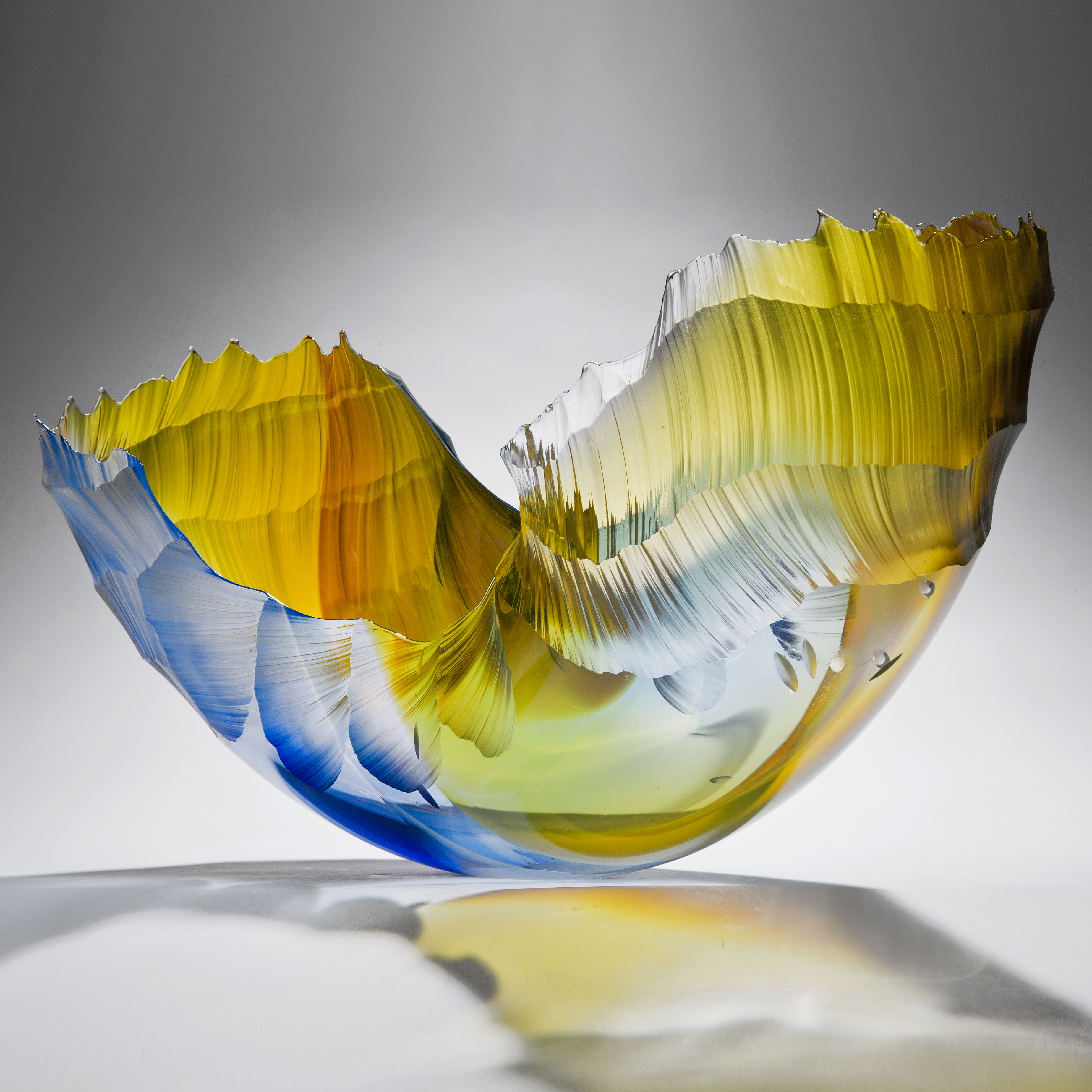 glass art sculpture in the shape of a wave in shades of yellow orange and blue