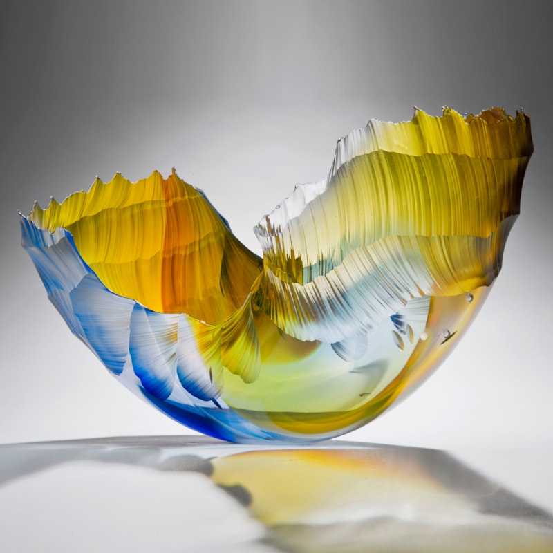 glass art sculpture in the shape of a wave in shades of yellow orange and blue