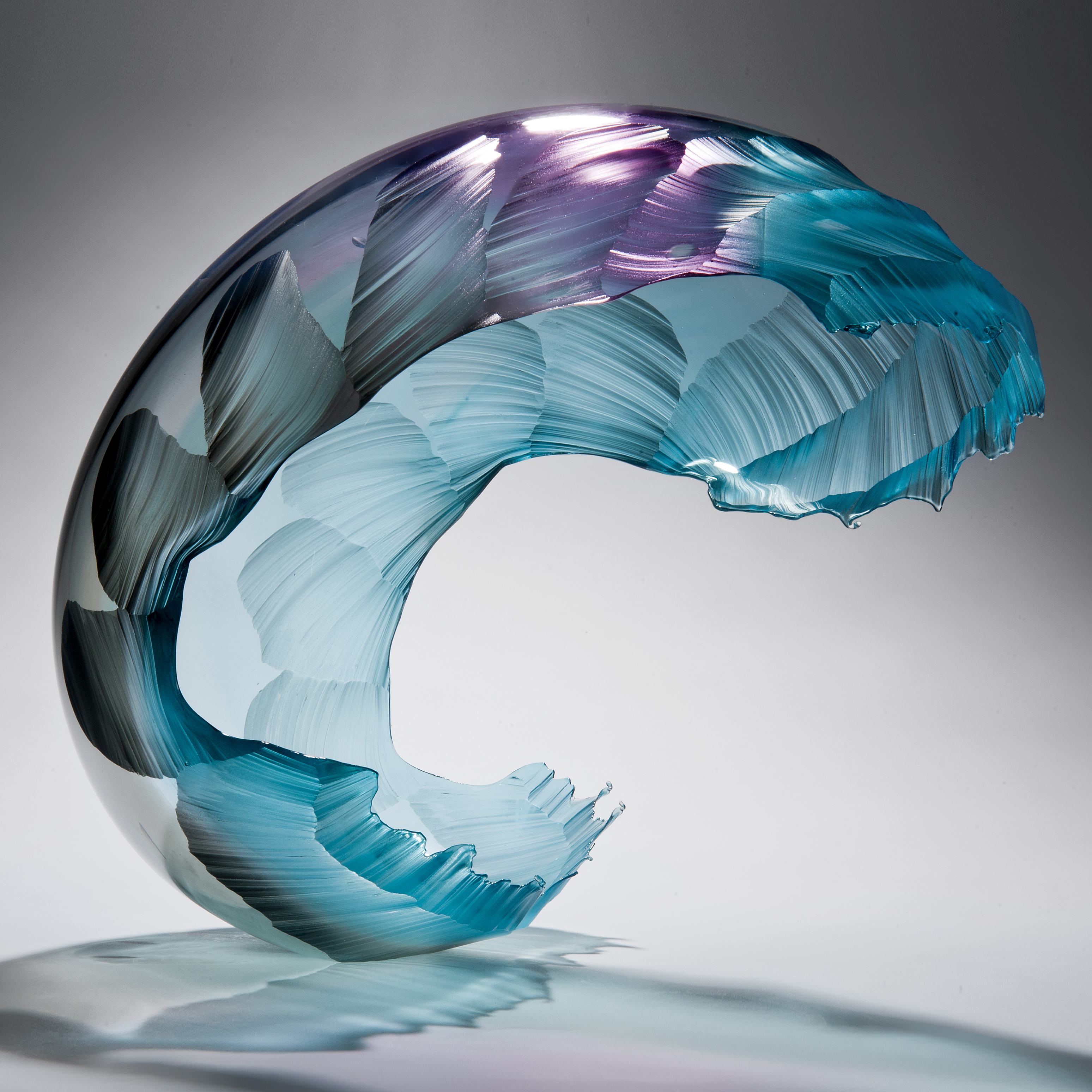 glass art sculpture in form of a wave in bright aqua blue with purple tint