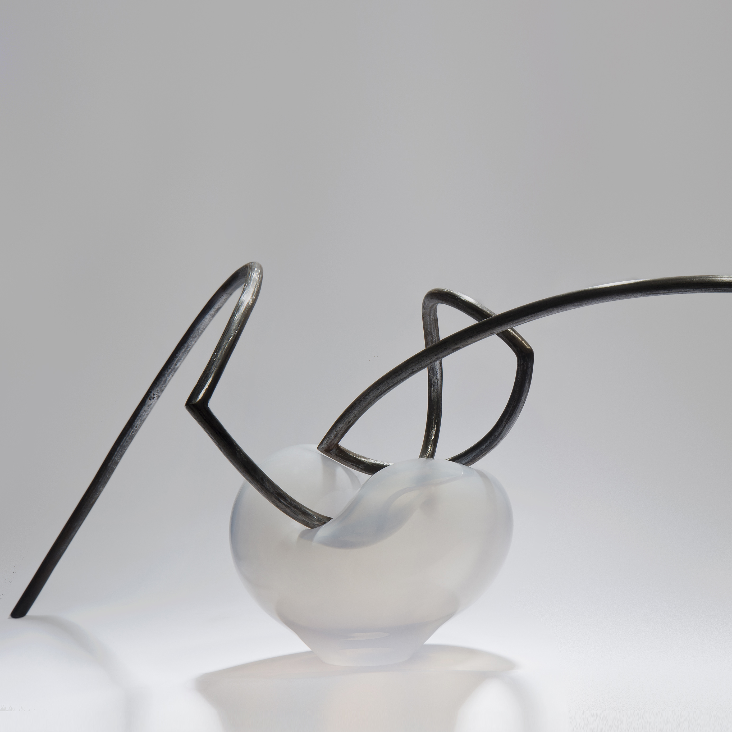 abstractly shaped pearl coloured glass dish with asymmetrical mangled thin black metal rod nestled in the centre