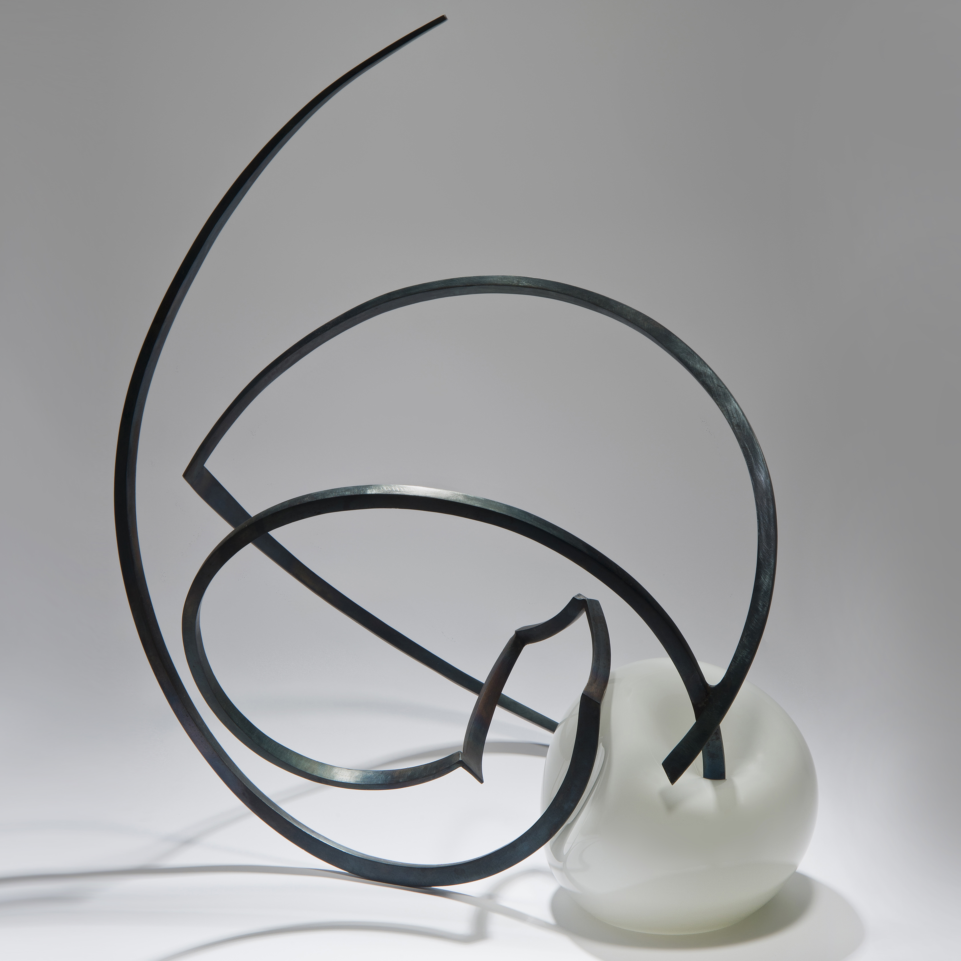 abstractly shaped pearl coloured glass sphere with asymmetrical mangled long thin black metal rod sprouting from the centre