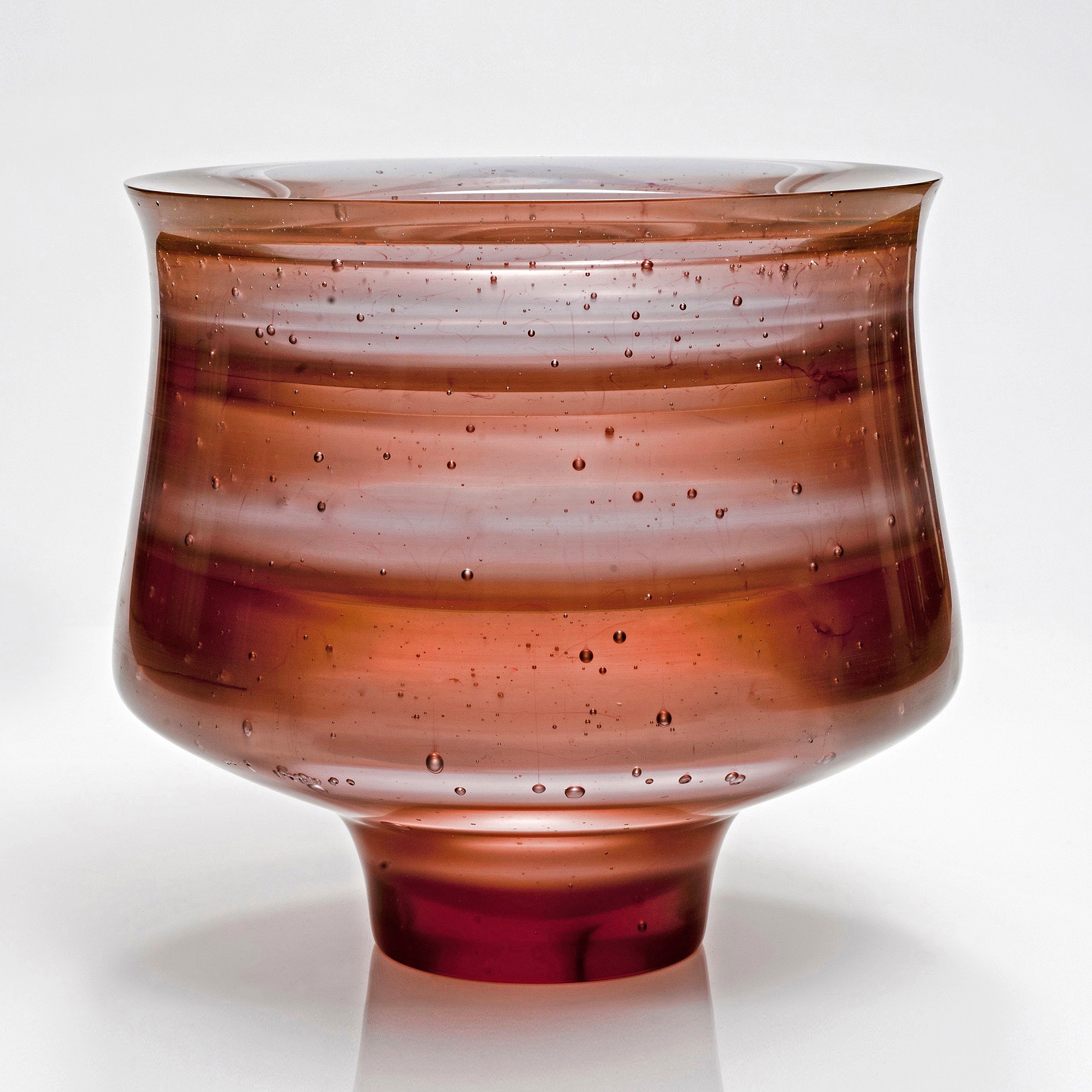 short sculpted glass vessel with open top in hues of brown with pattern resembling jupiter