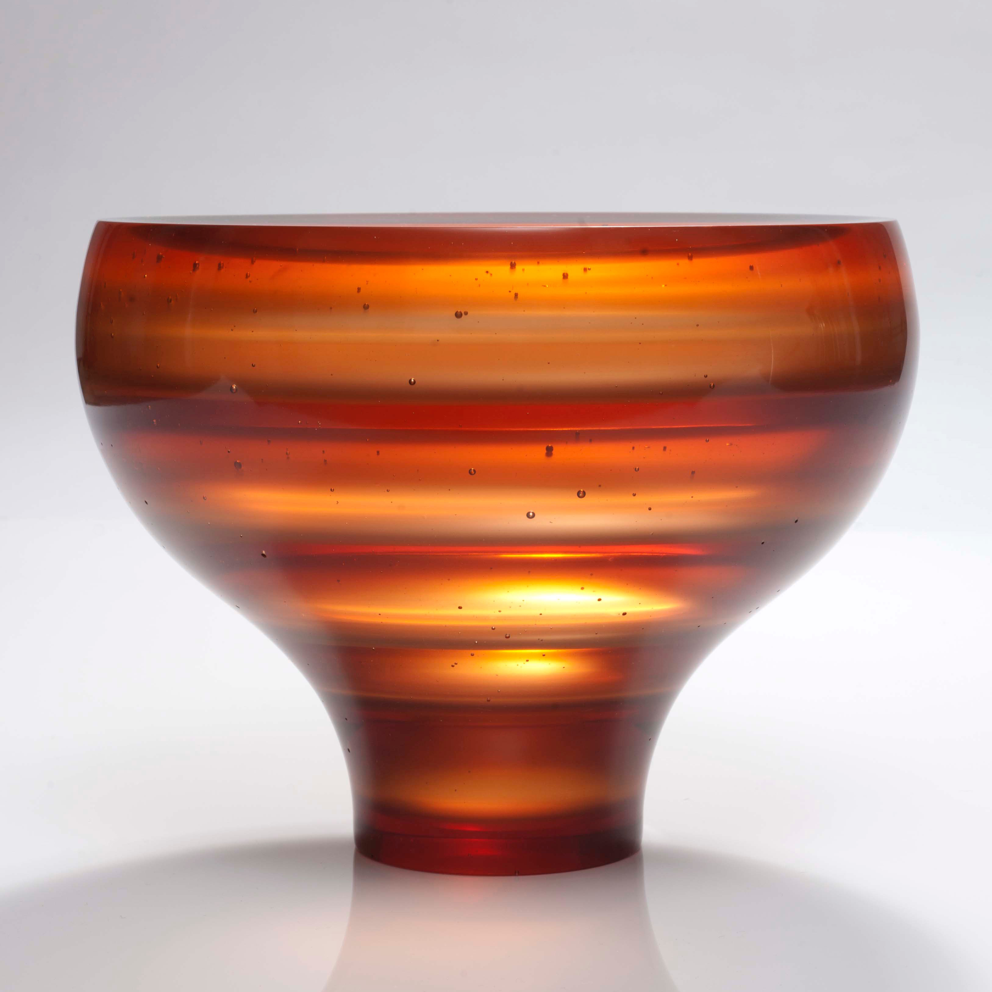 sculpted glass vessel with thin base and wide top with horizontal lined patters in orange shades