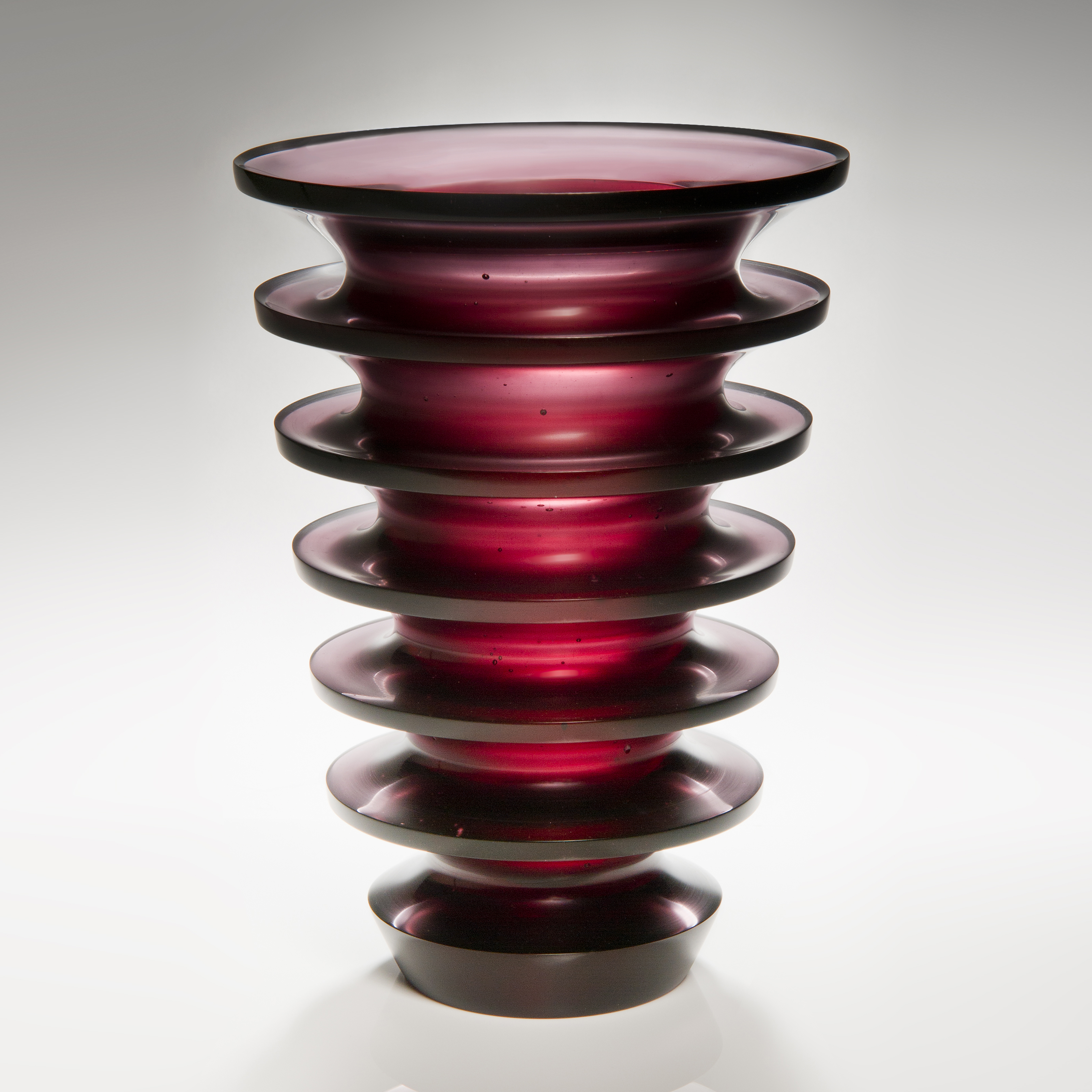 tall dark red art glass sculpture with geometrically positioned rings