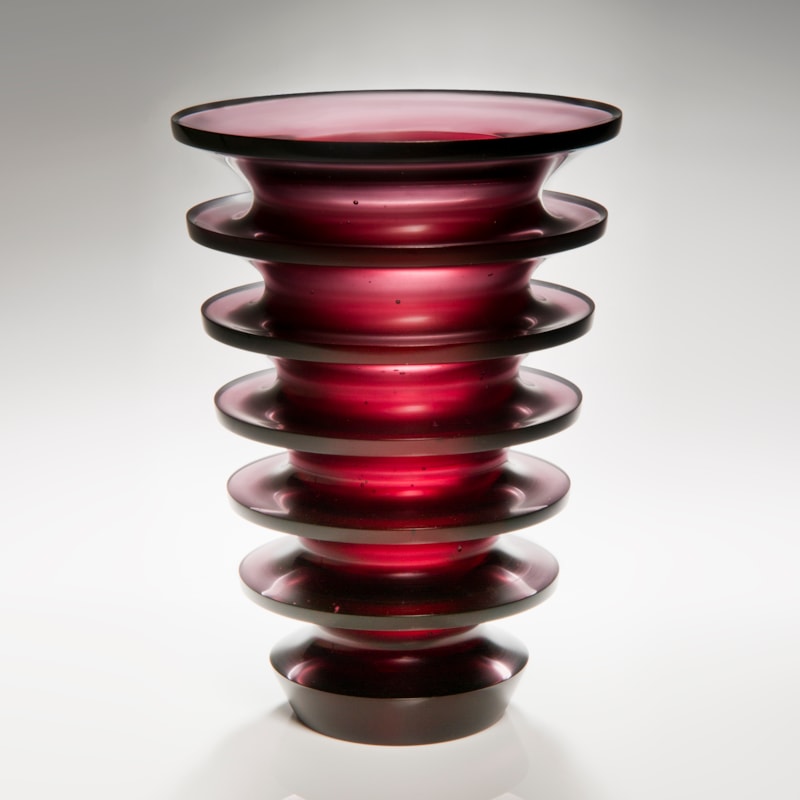 tall dark red art glass sculpture with geometrically positioned rings