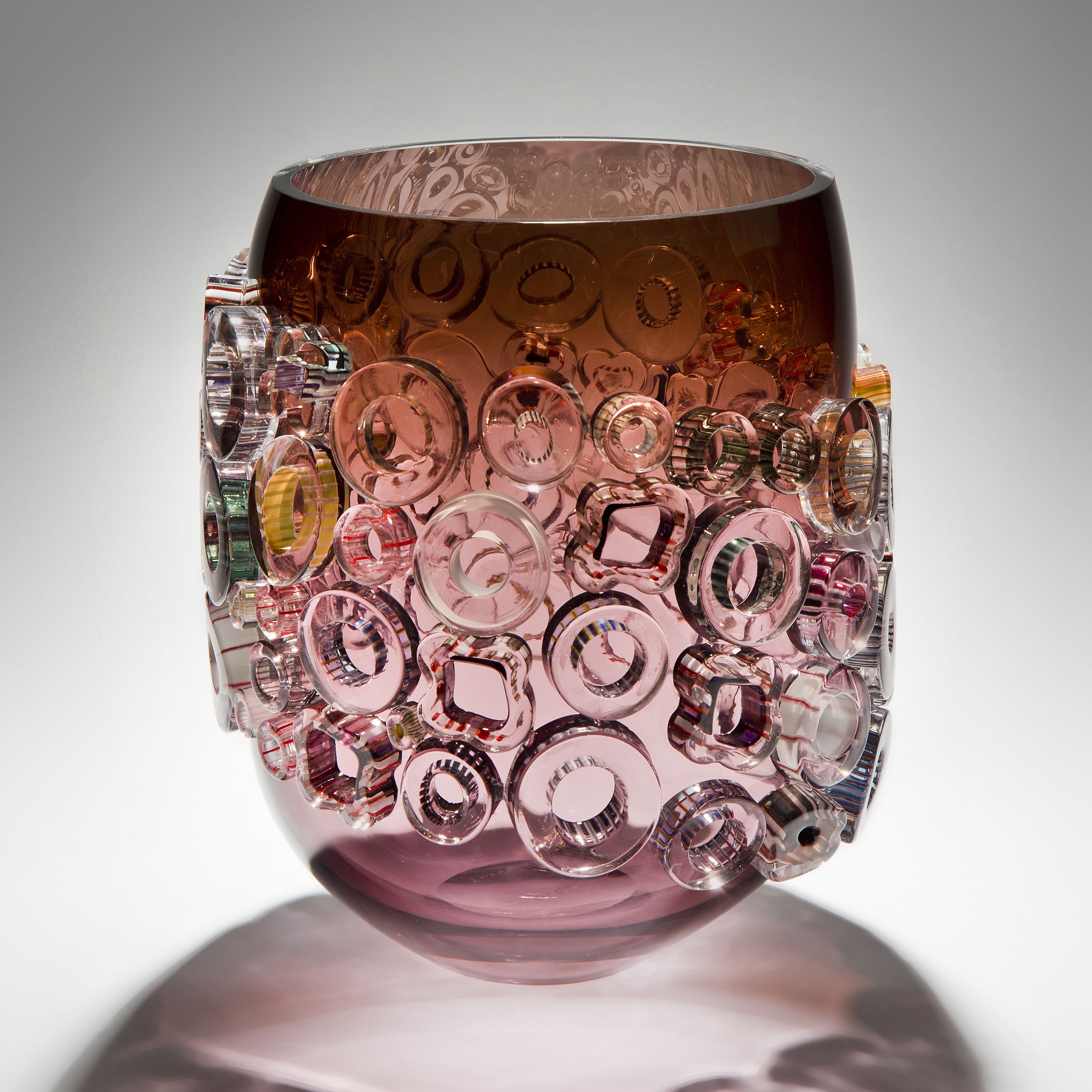pink sculpted glass vase artwork with pink yellow and green circular patterns on exterior