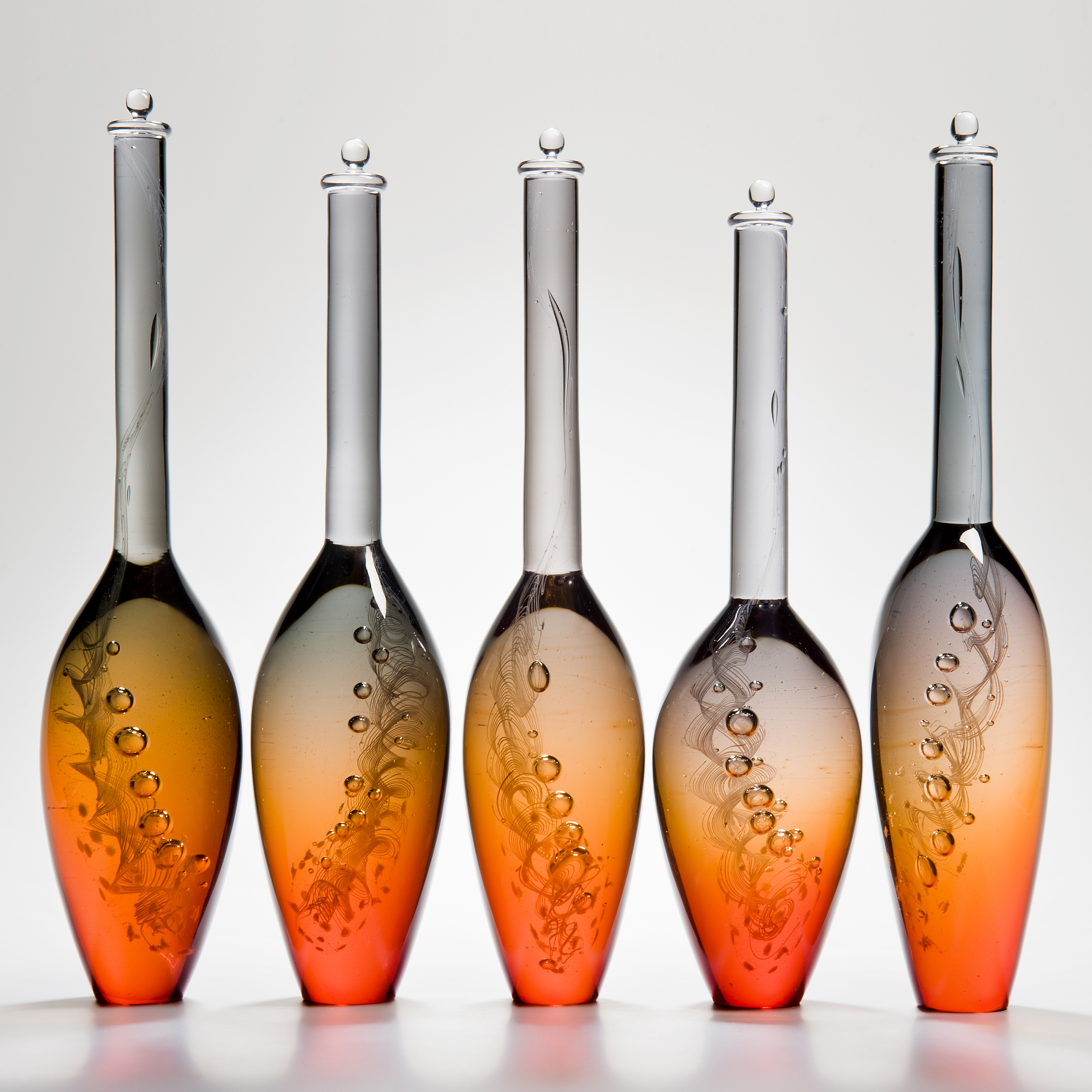 five bright orange modern glass vase sculptures with tall grey necks and engraved pattern