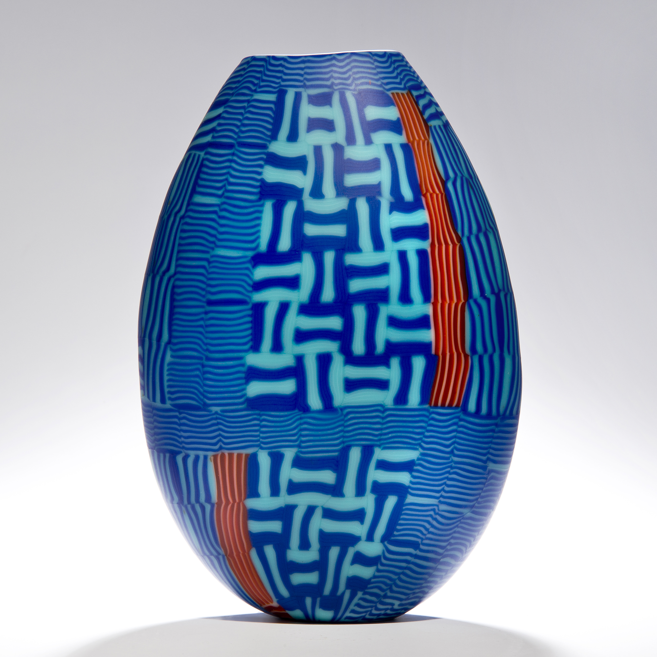 sculpted glasss vessel in oval shape with lined patterns in blue turquoise and orange