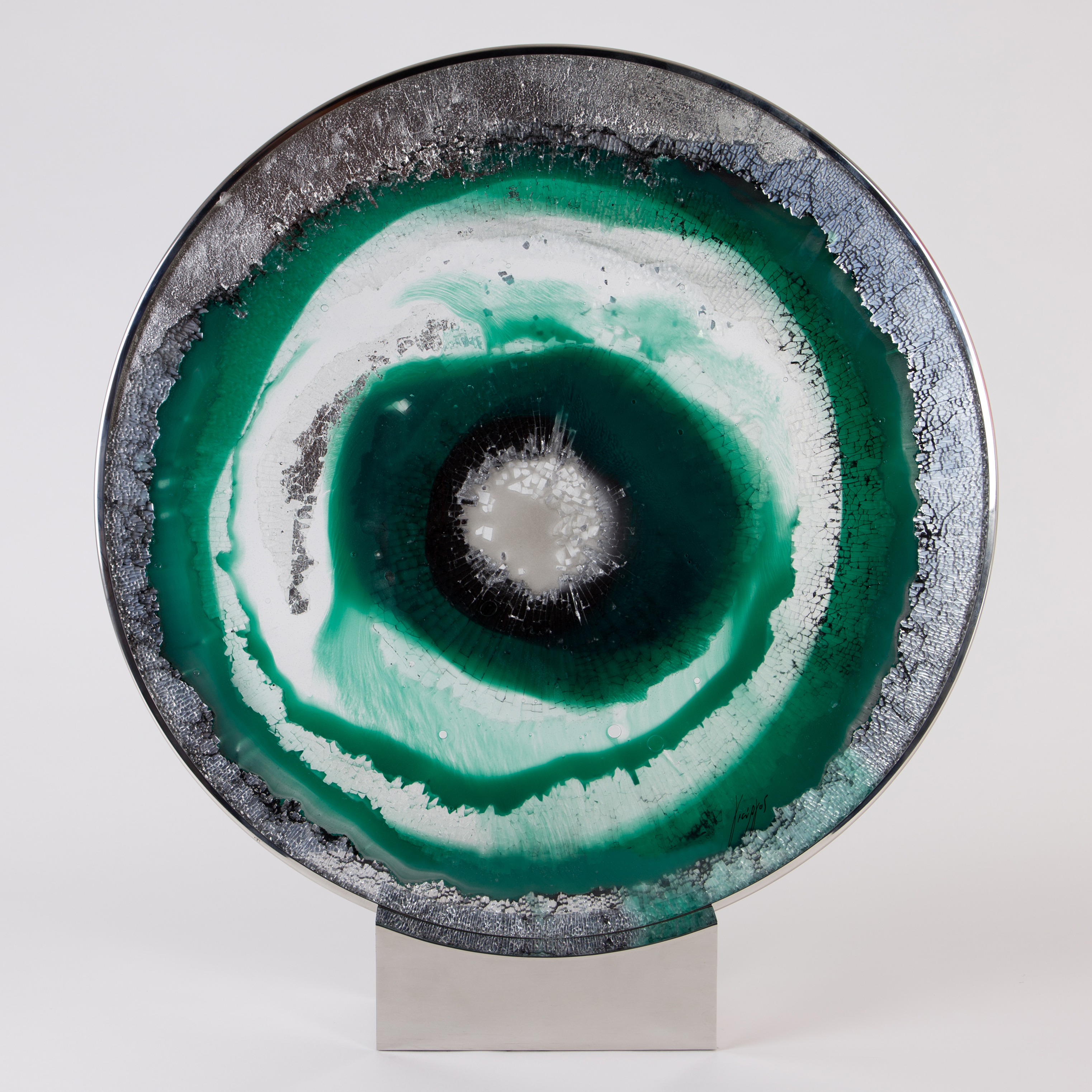 glass and steel sculpted circle with green silver and black swirls forming pattern of an eye