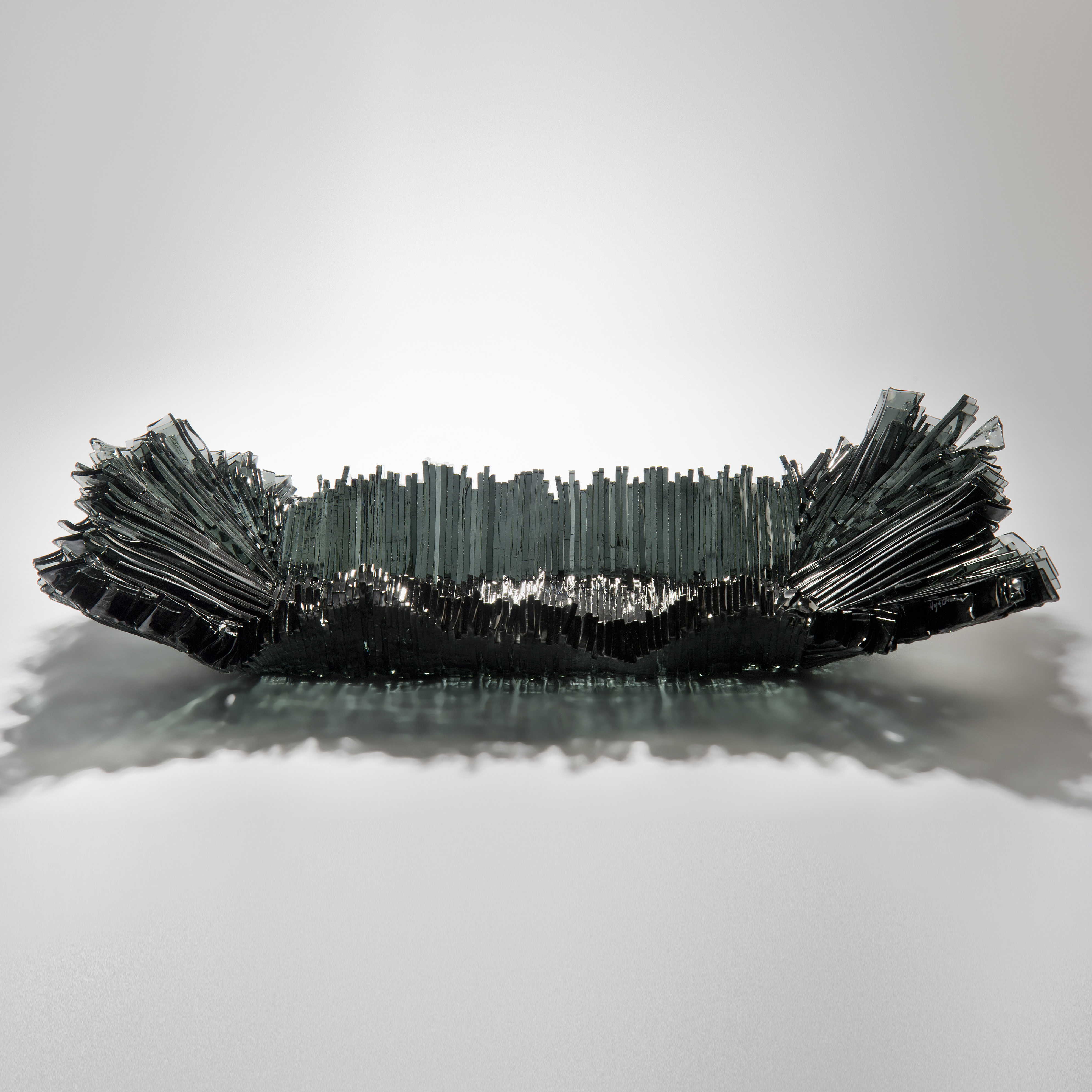 modern art-glass sculpture with hundreds of long thin dark grey shards arranged around edge to form bowl 