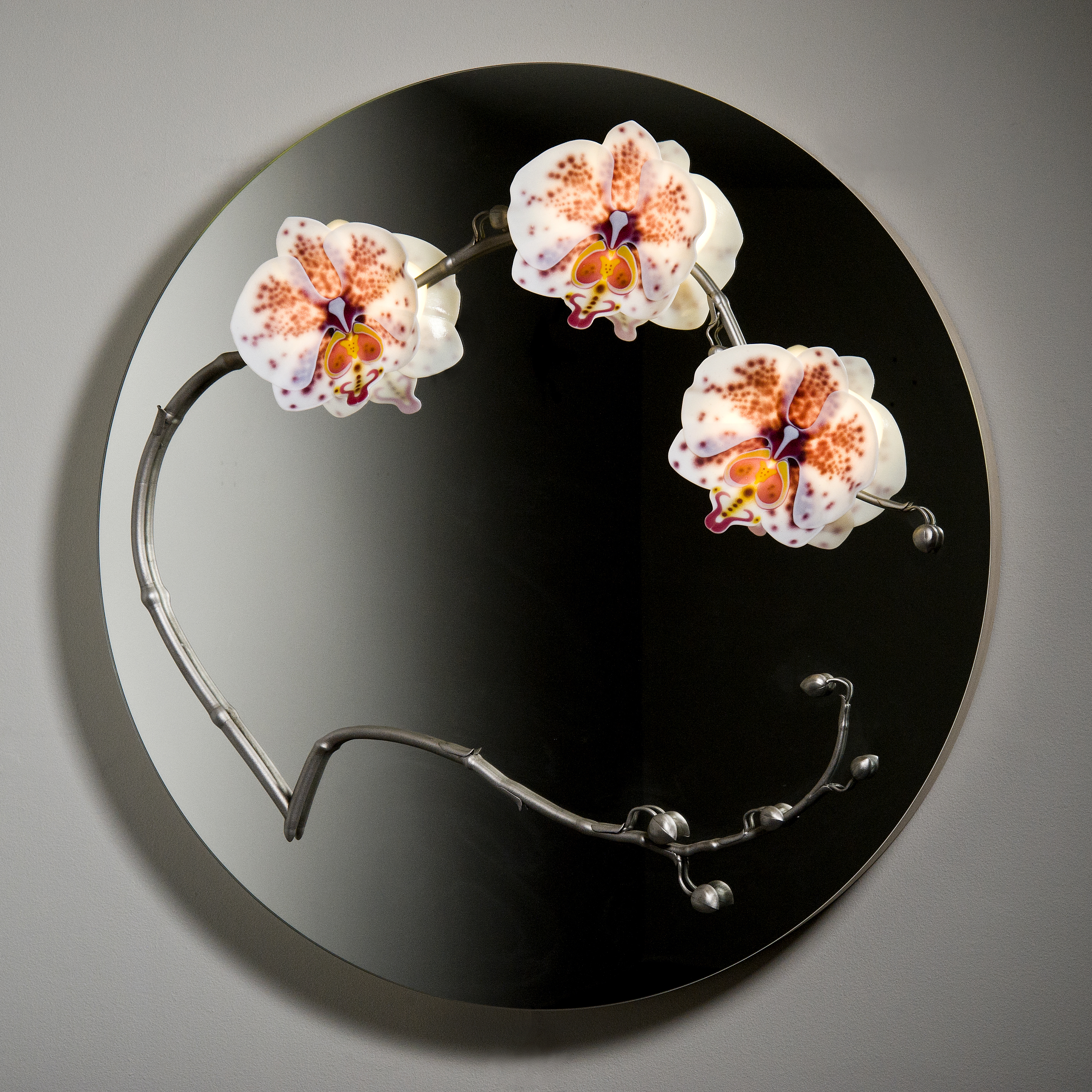 round black glass mirror with three sculpted glass orchids
