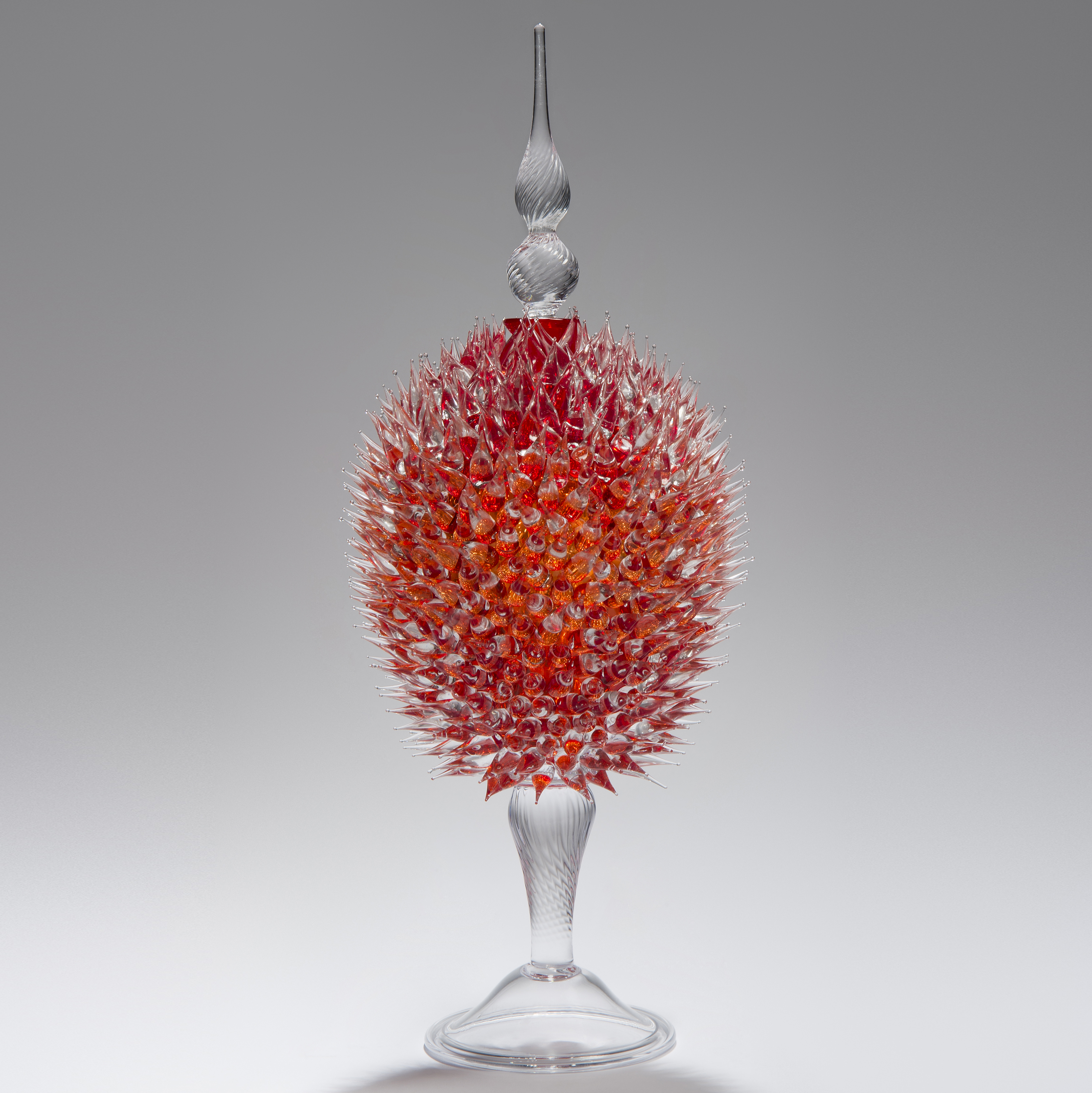 glass sculpture of spiked cherry red ball in the centre of clear glass base and top