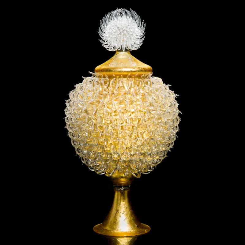 gold glass sculpture of round jar atop cone shaped base with white thistle top