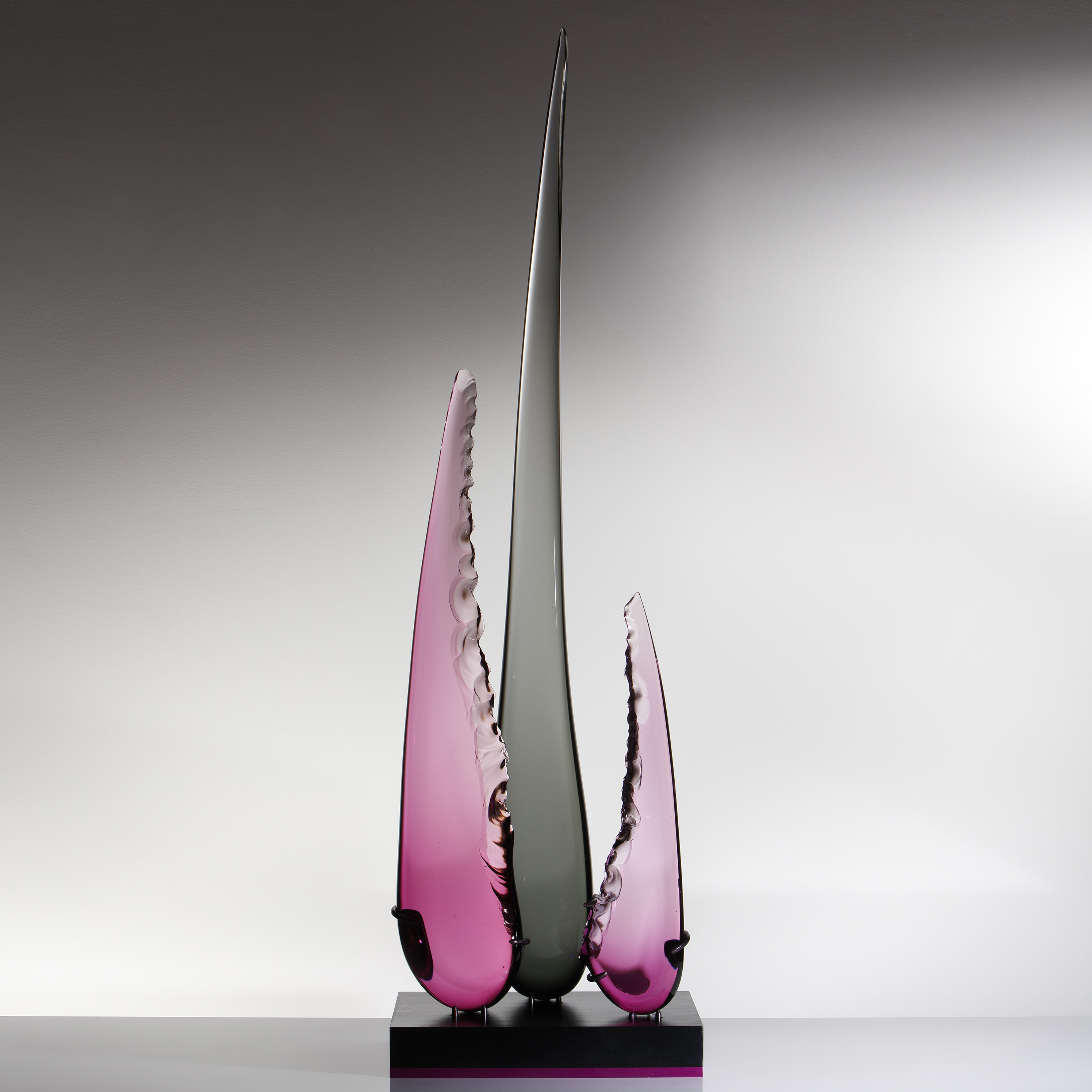 abstract sculpted glass artwork of three long glass shards one long black in the centre and two shorter in purple to either side