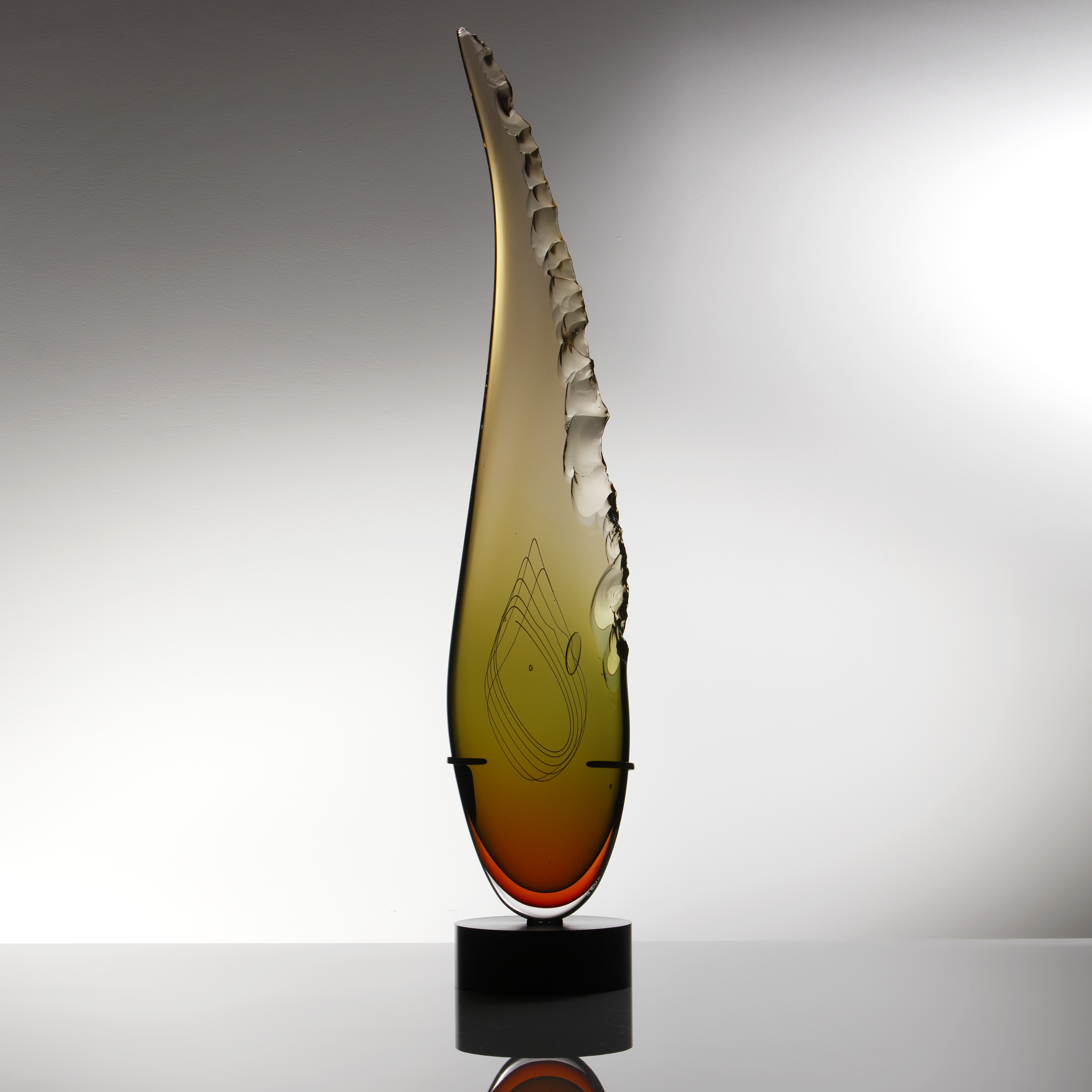 sculpted amber glass in upright feather shape resting on black base