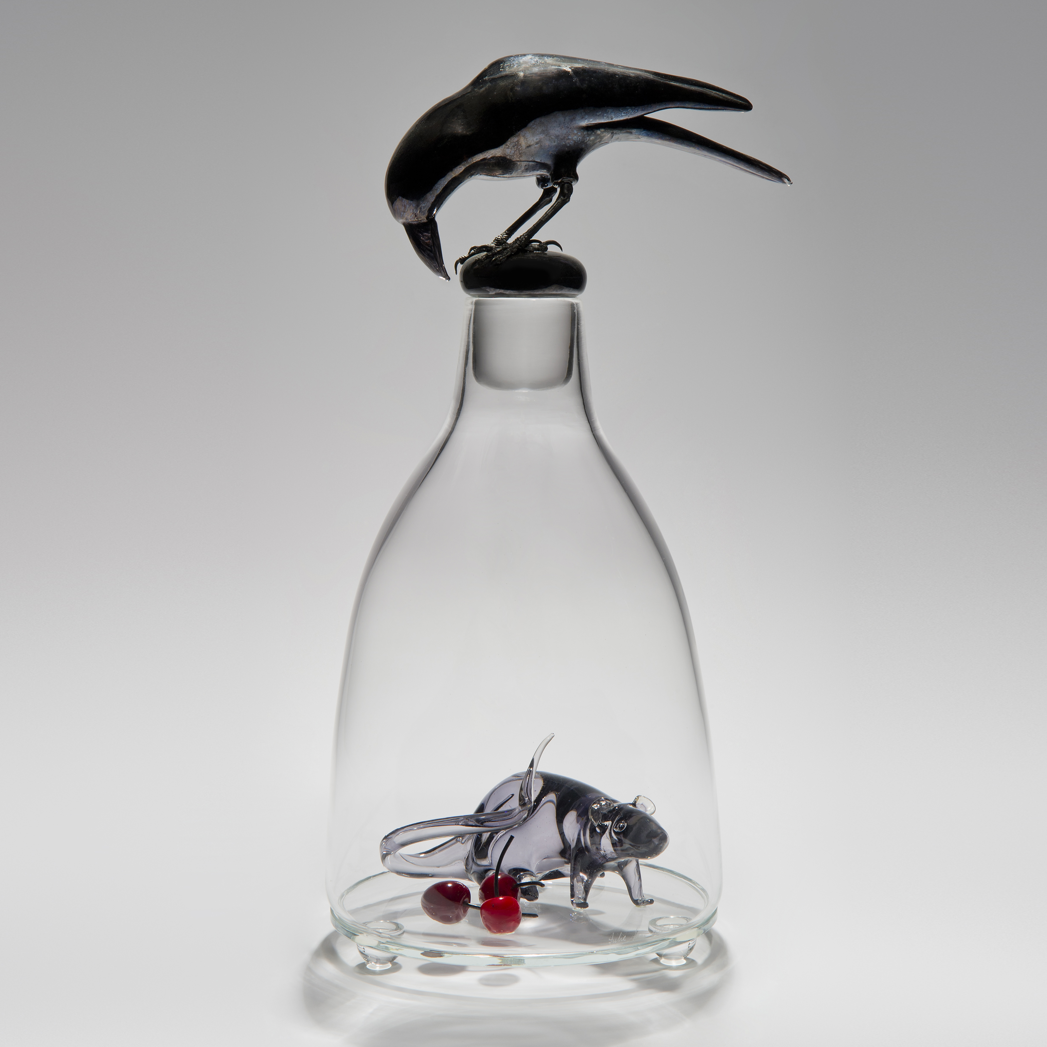 glass and steel sculpture of a mouse trapped in a clear glass flask with a crow peering in from the top