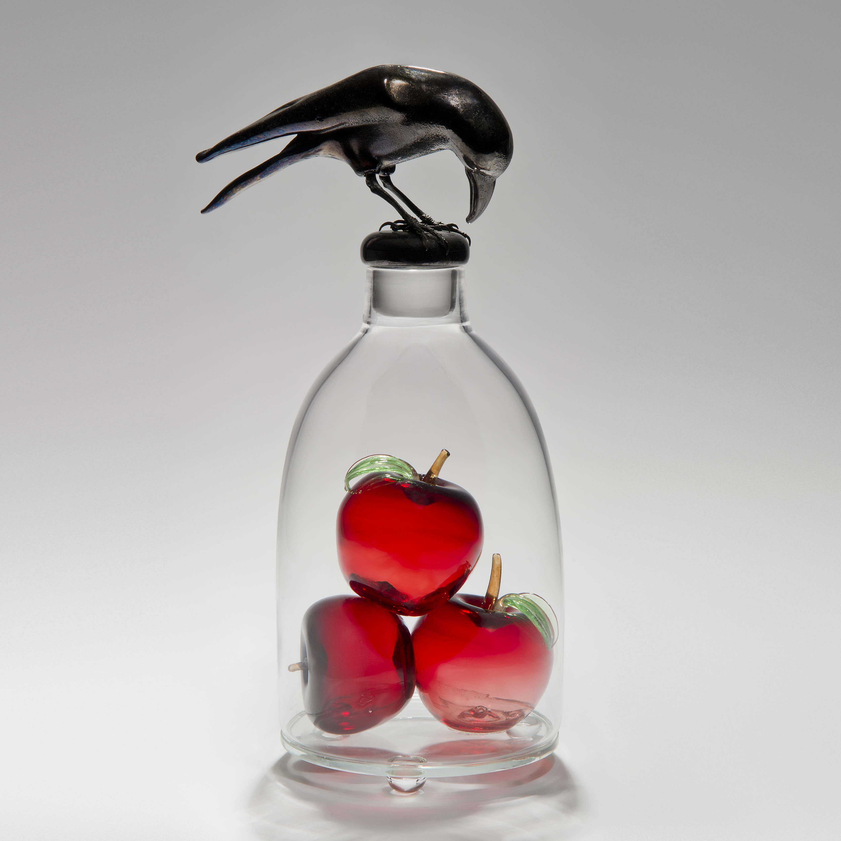 glass and steel sculpture of three apples inside glass container with a crow peering on top looking in