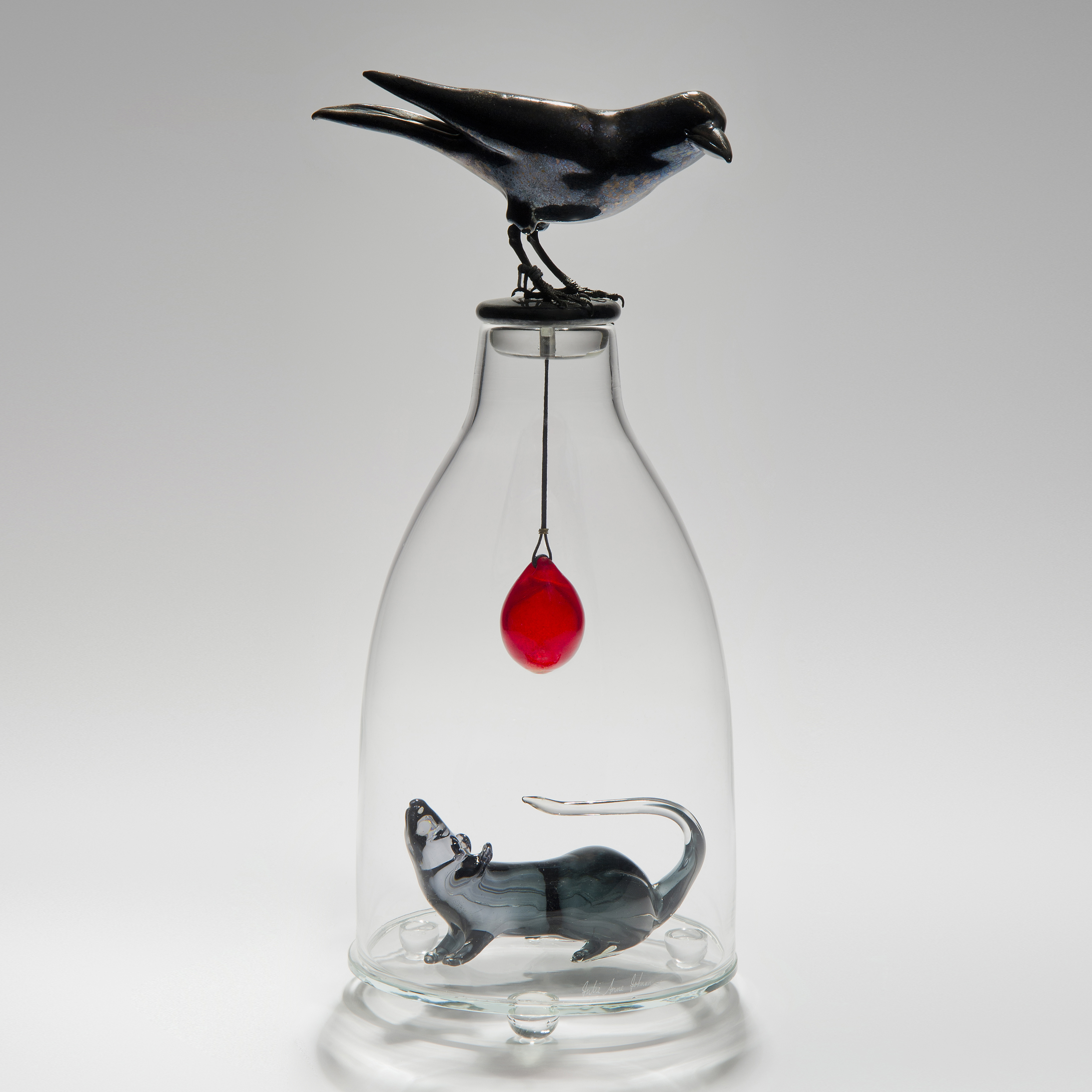 glass and steel sculpture of a mouse trapped in a clear glass flask with a crow resting on top