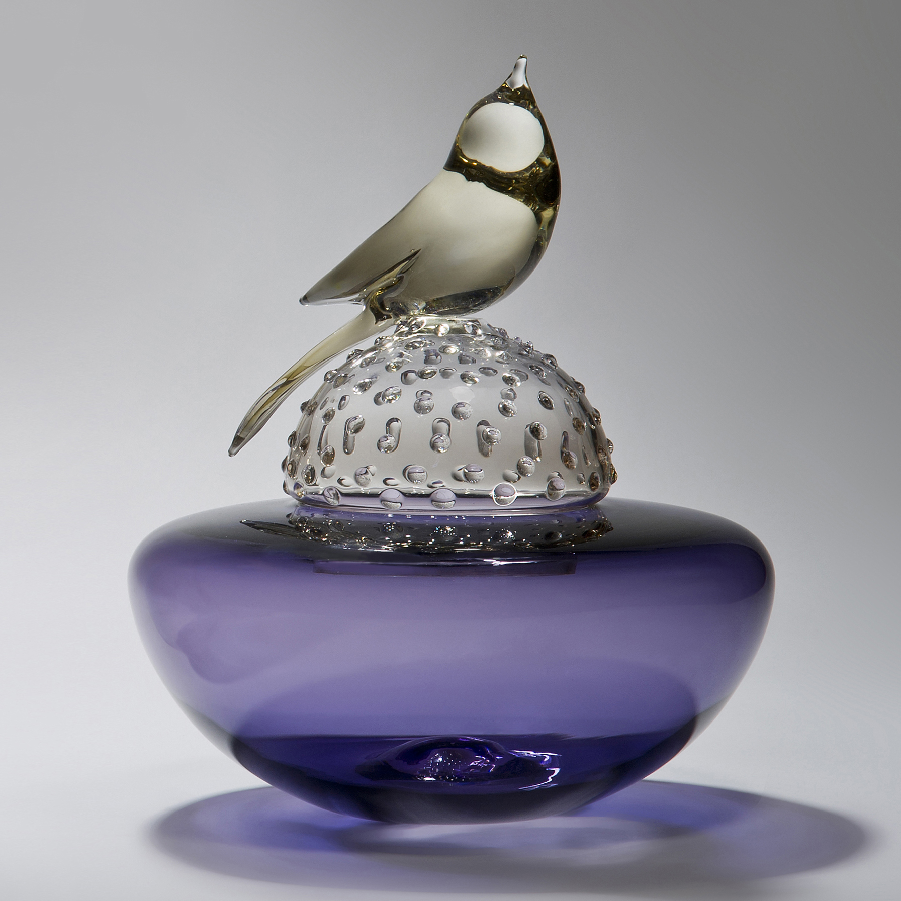glass artwork of a light grey bird resting on a bright purple funeral urn