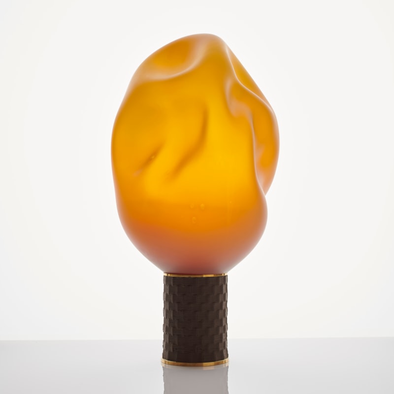 abstract yellow and orange blown flame-shaped glass ornament resting on bronze base