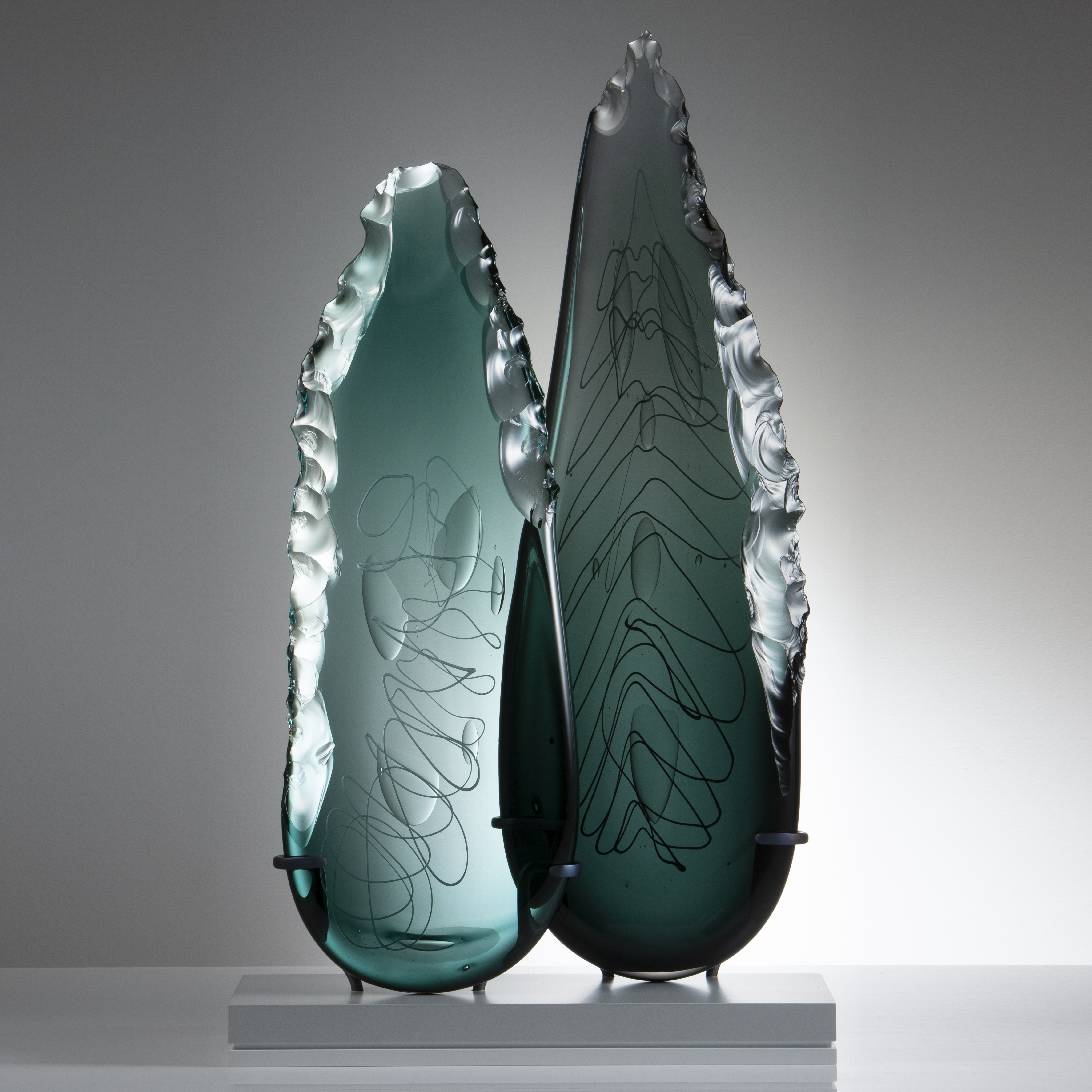 two leaf-shaped glass art sculptures in aqua and jade on clear rectangular base