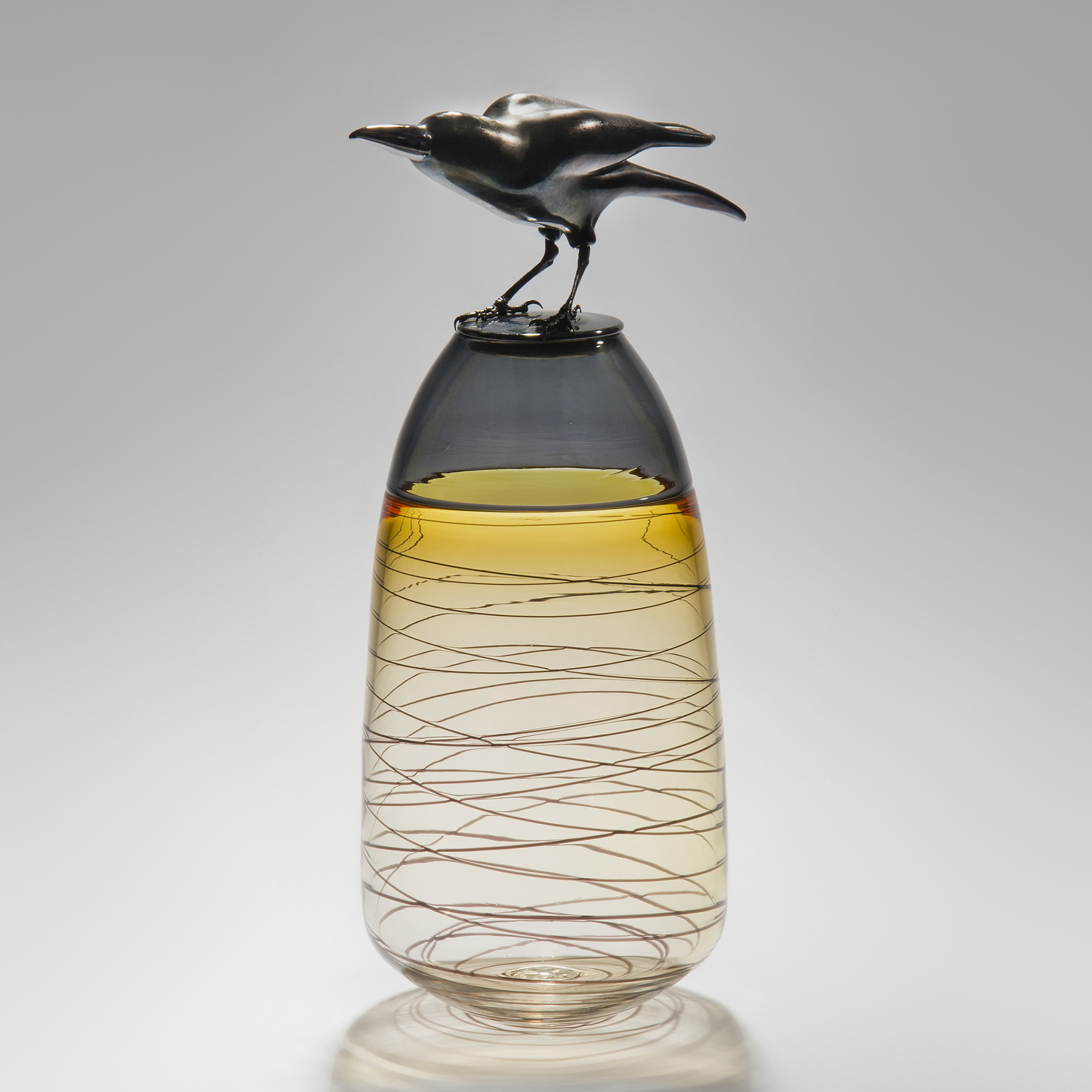 glass and steel sculpture of a crow atop a clear and yellow tinted vase with helter skelter pattern