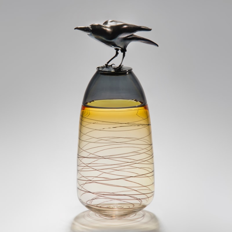 glass and steel sculpture of a crow atop a clear and yellow tinted vase with helter skelter pattern