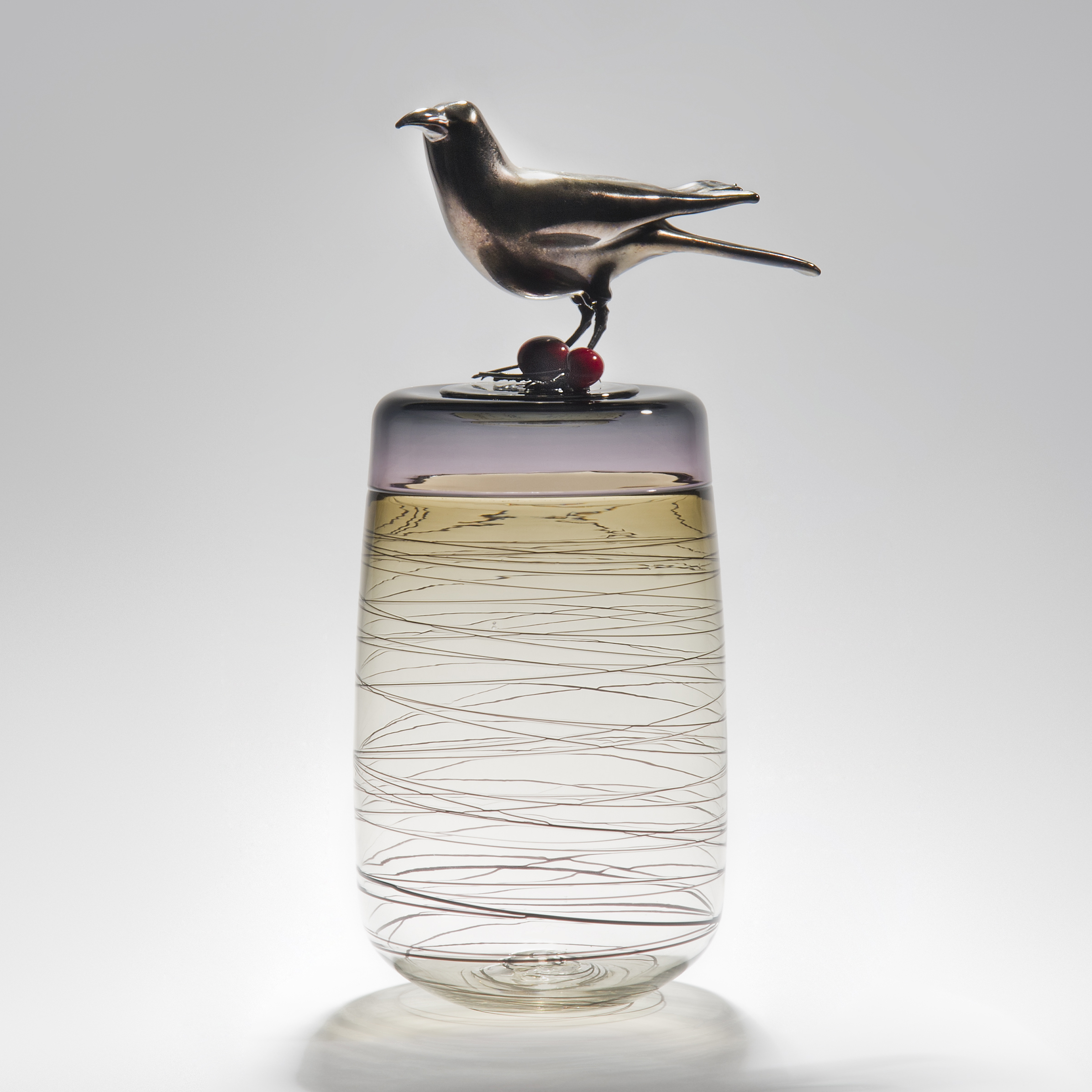 sculpted clear glass vase with angled lines circling exterior with stainless steel crow sitting atop with cherries at its feet