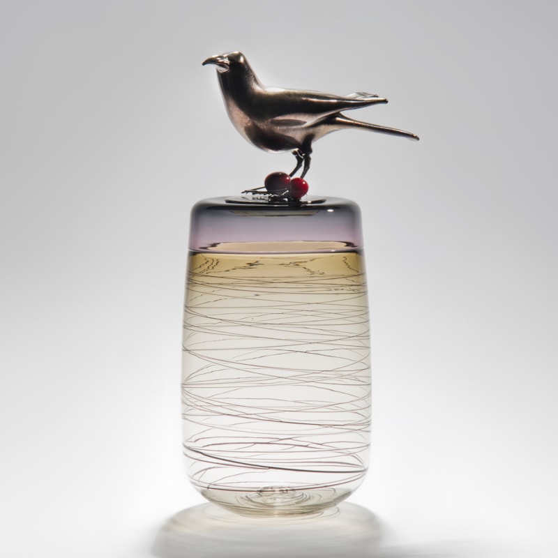 sculpted clear glass vase with angled lines circling exterior with stainless steel crow sitting atop with cherries at its feet