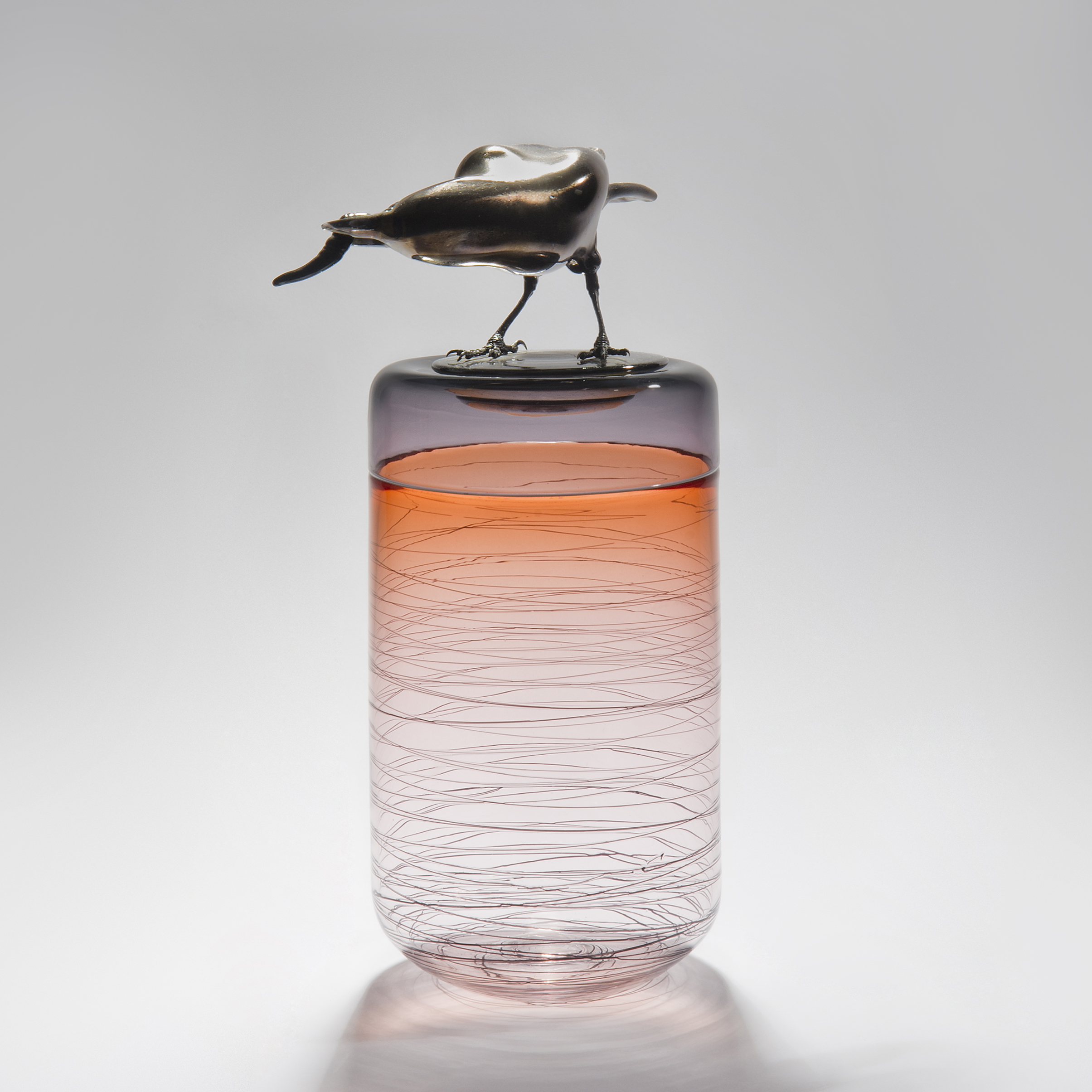 sculpted glass vase in clear and orange with faint lines encircling exterior with stainless steel crow on top 