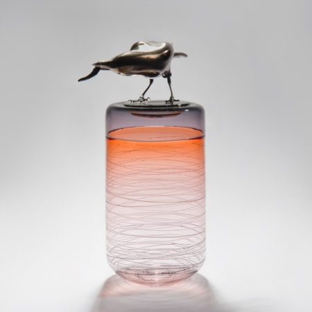 sculpted glass vase in clear and orange with faint lines encircling exterior with stainless steel crow on top
