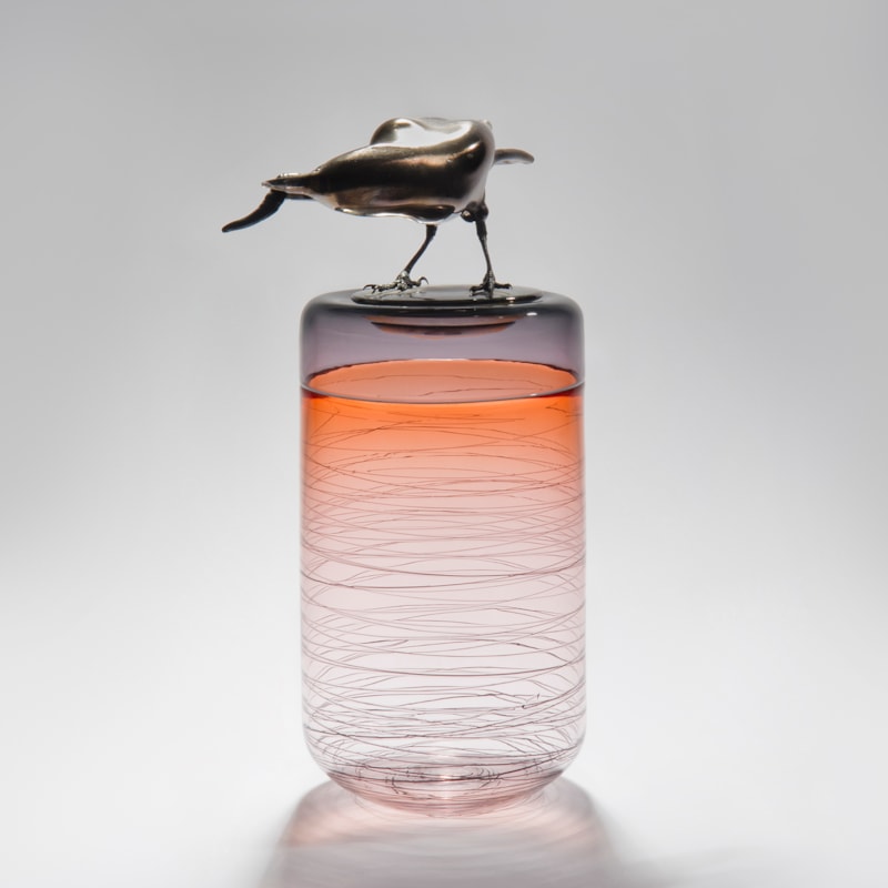 sculpted glass vase in clear and orange with faint lines encircling exterior with stainless steel crow on top