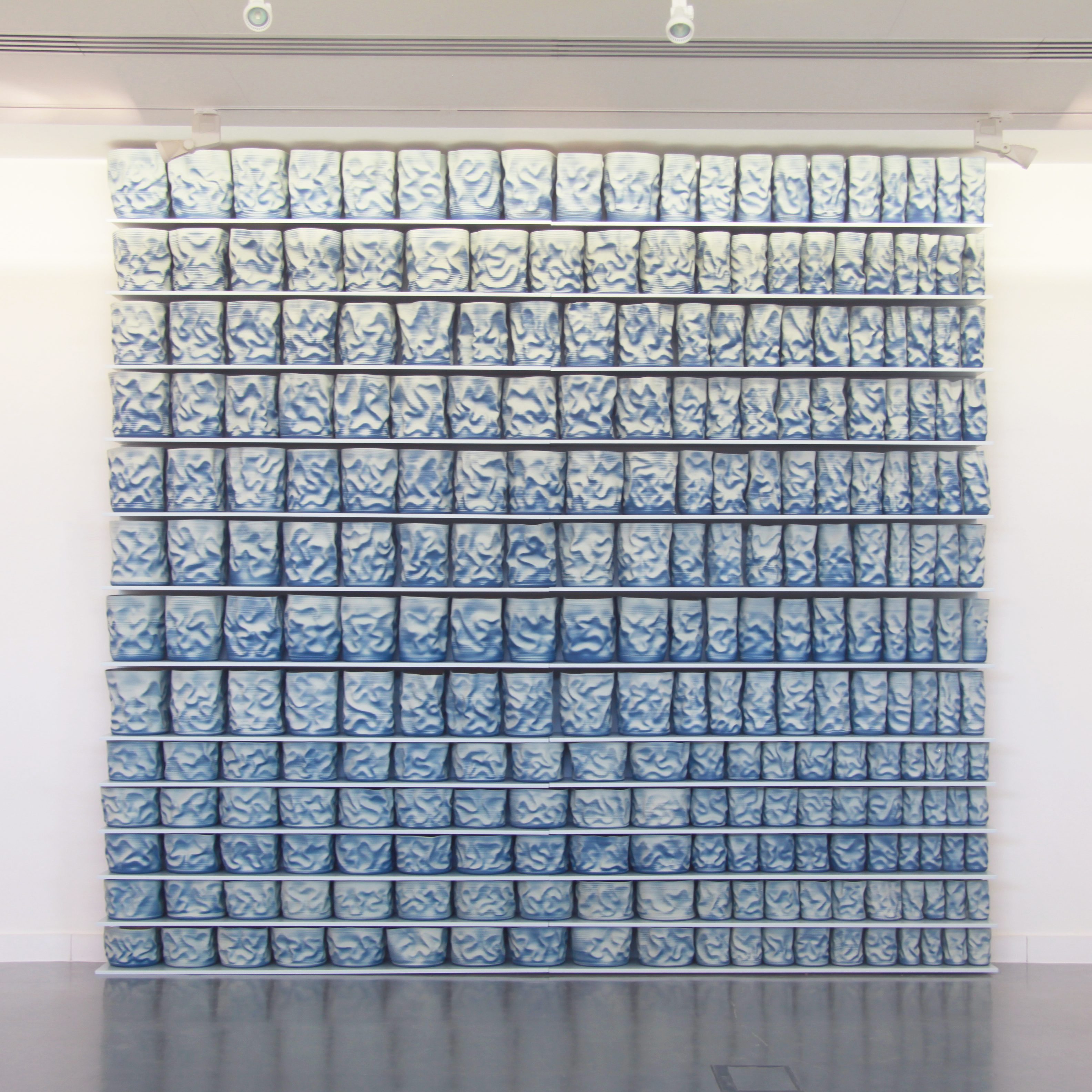 shelves of blue and cream scrunched and wrinkled looking hand thrown ceramic vessels creating a large wall mounted sculptural installation