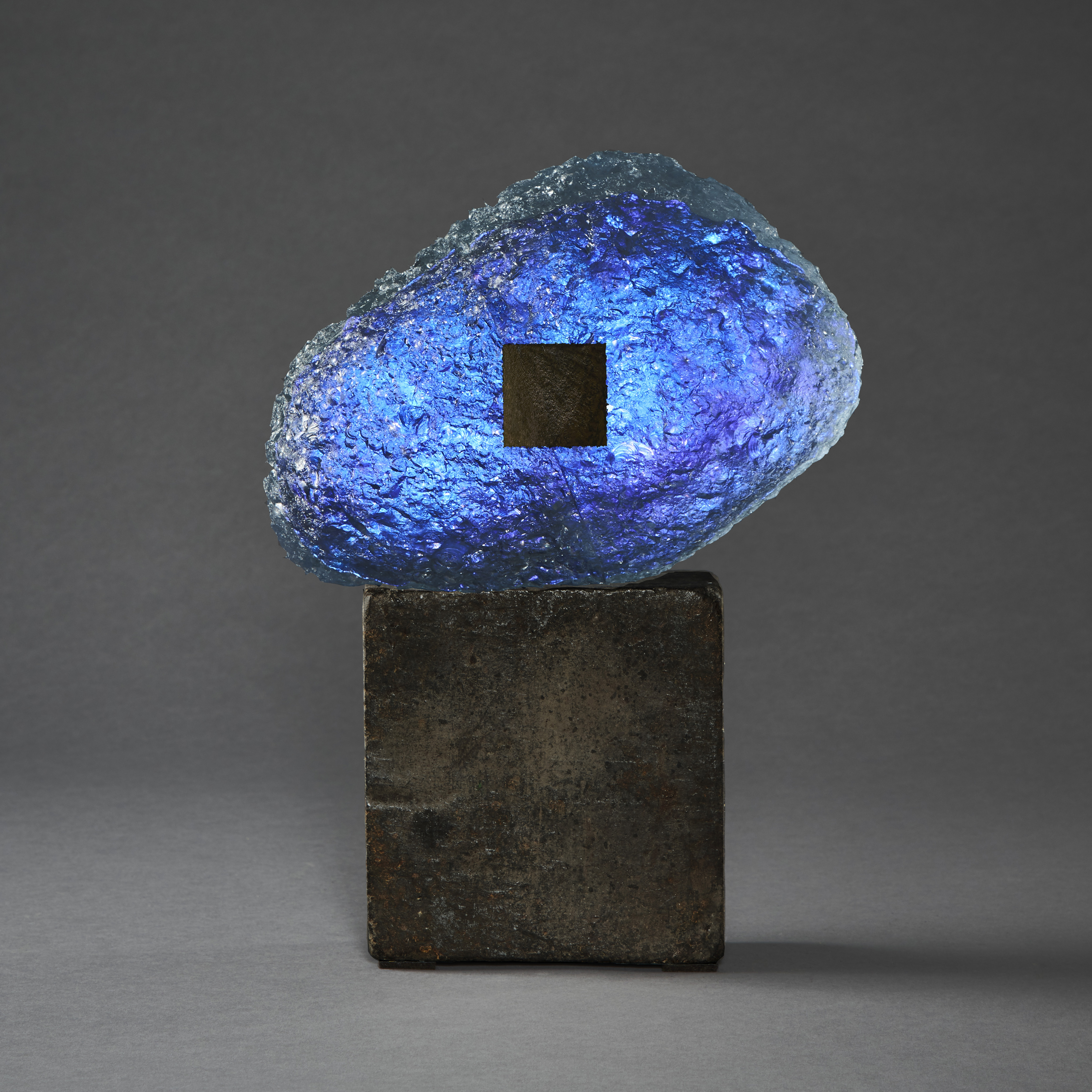blue and dark brown meteoric hand formed glass amorphic sculpture on a weather cube base made steel