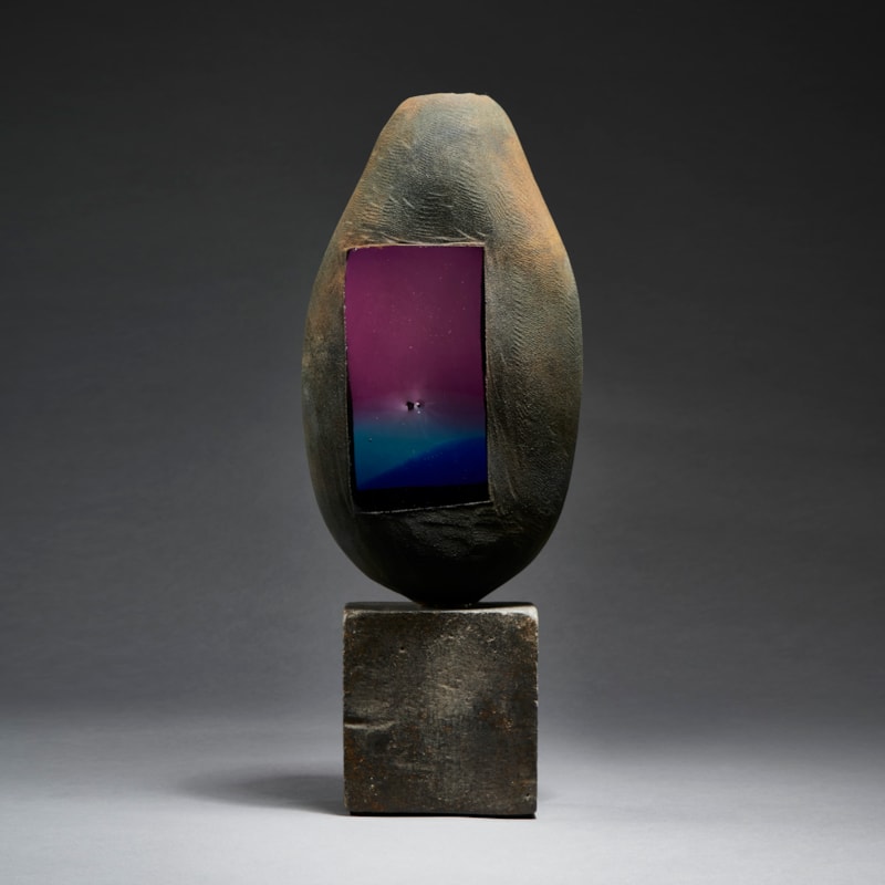 grey and brown rustic battered looking ovoid handmade glass sculpture with faded blue to purple glass window on a beaten metal cube base