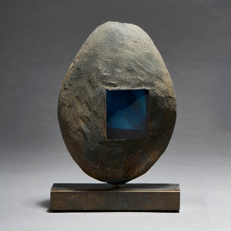 grey and brown hand made glass and metal ovoid shaped sculpture with square glass blue window and square geometric aged metal base