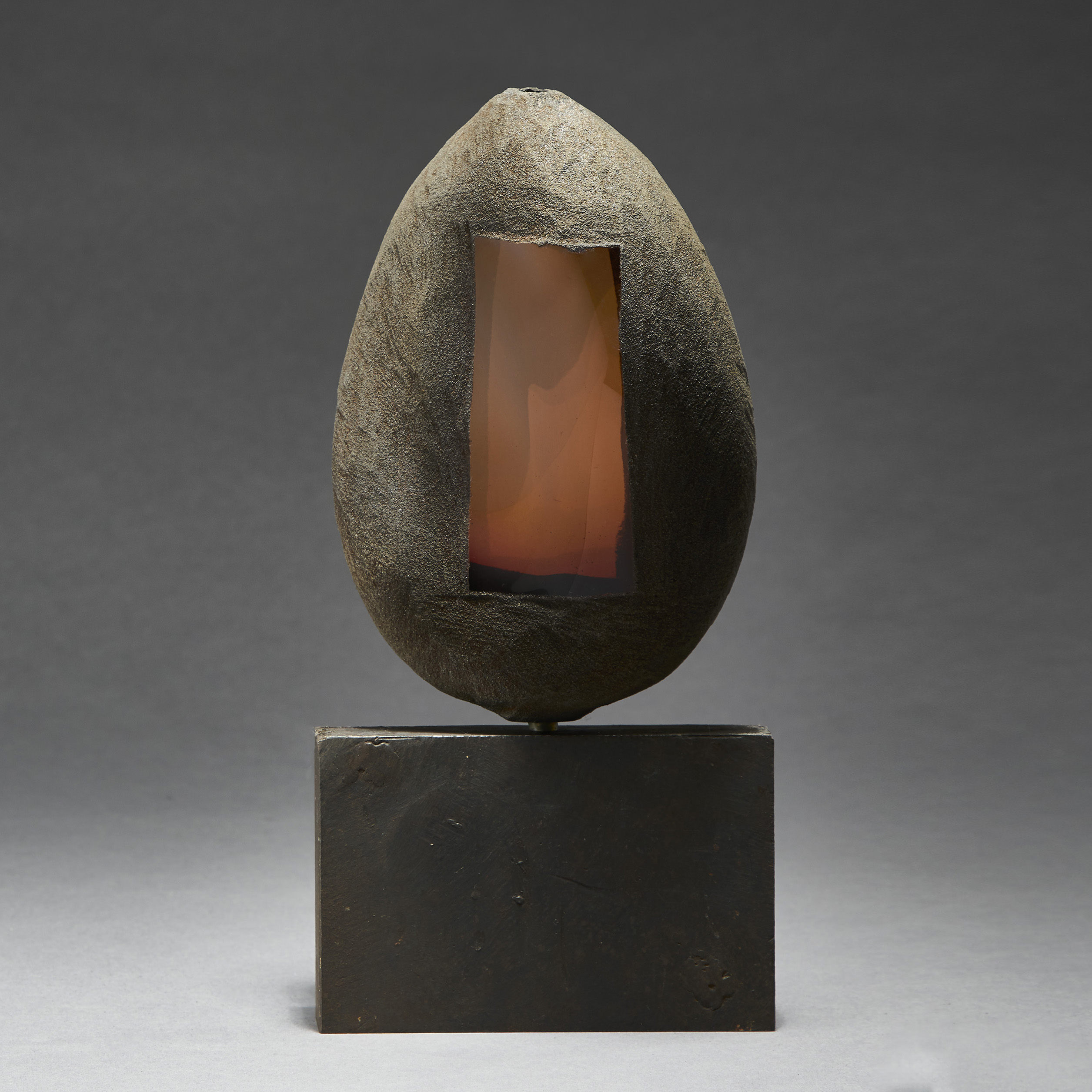 grey and brown hand made ovoid shaped glass and metal sculpture with square geometric aged metal base and rectangular orange glass window