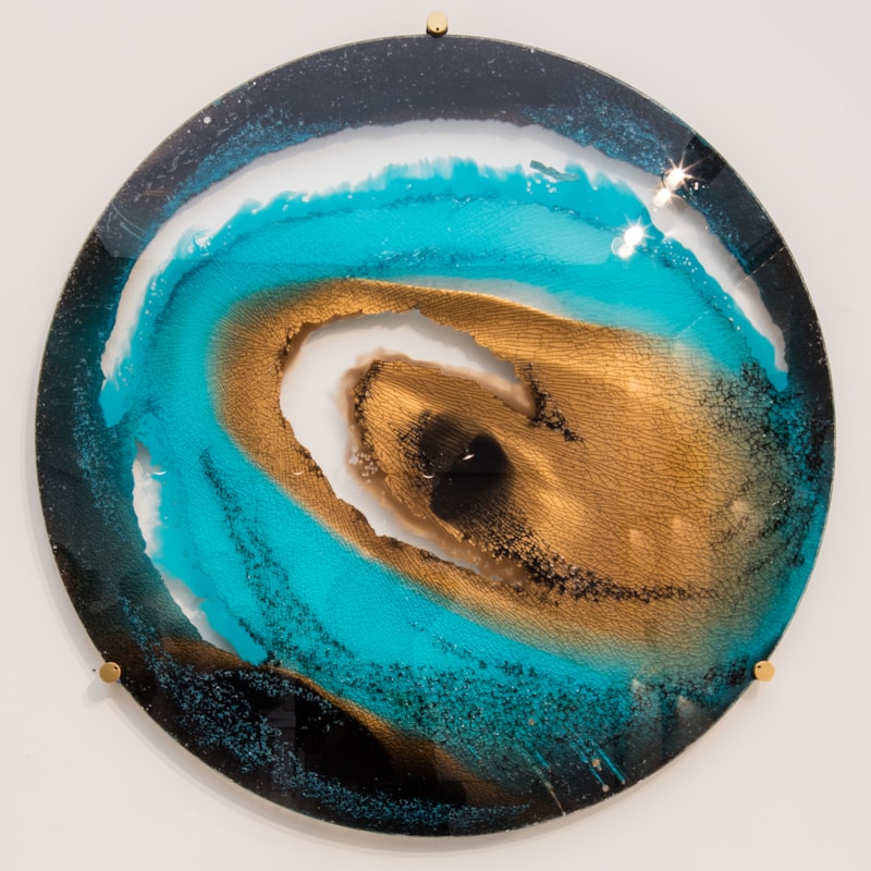 round glass art sculpture of eye-like shape in shades of blue and sand