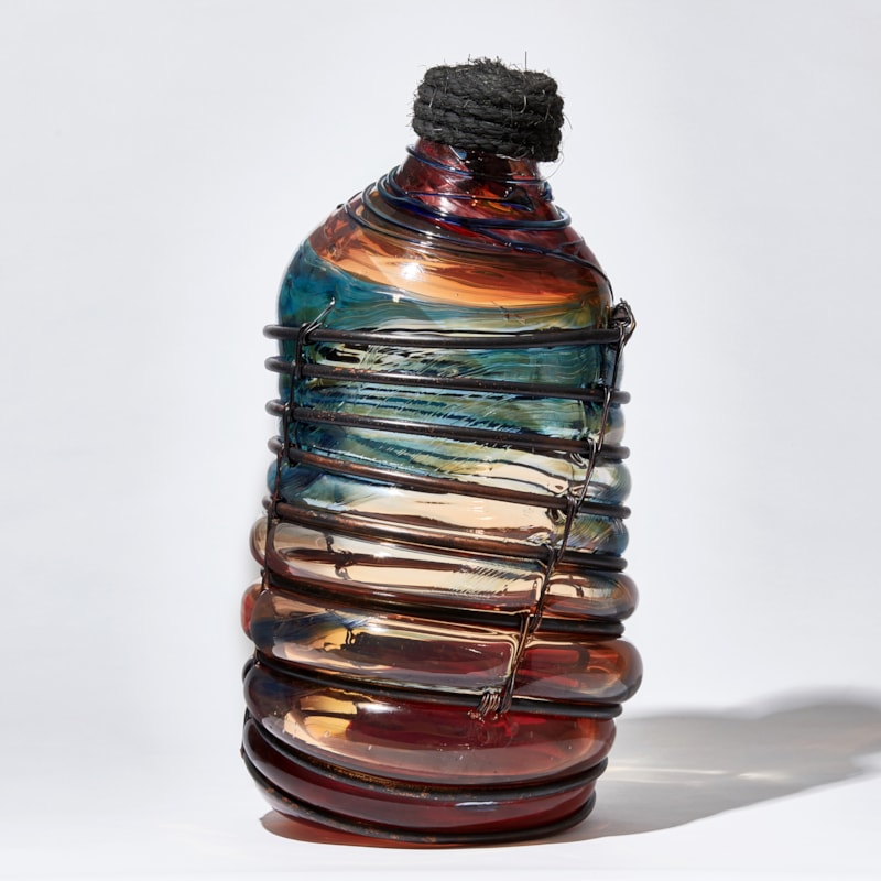 red blue and brown metal caged leaning bottle shaped glass sculpture with rope stopper detail