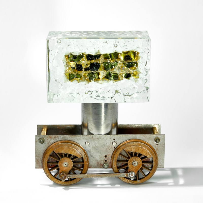 chunky ages metal train chassis with solid rectangular mass of glass above with inner winking eyes handmade from glass